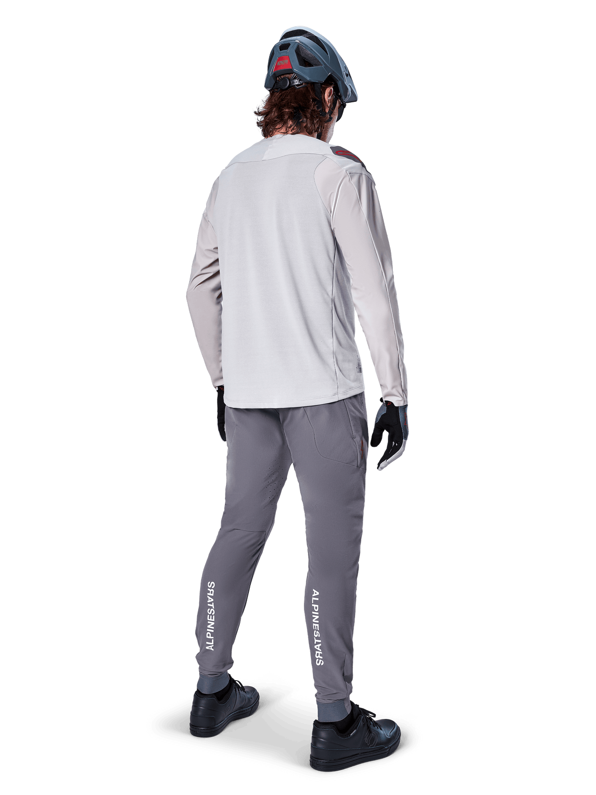 Alpinestars A-Aria Elite Hose, MTB-Fahrradhose, Dunkelgrau, Rückansicht eines Fahrers in kompletter Ausrüstung, mit weißem Alpinestars-Branding an den Unterschenkeln, Performance-Passform mit Laserperforationen, kombiniert mit einem hellgrauen Langarmtrikot und grauem MTB-Helm