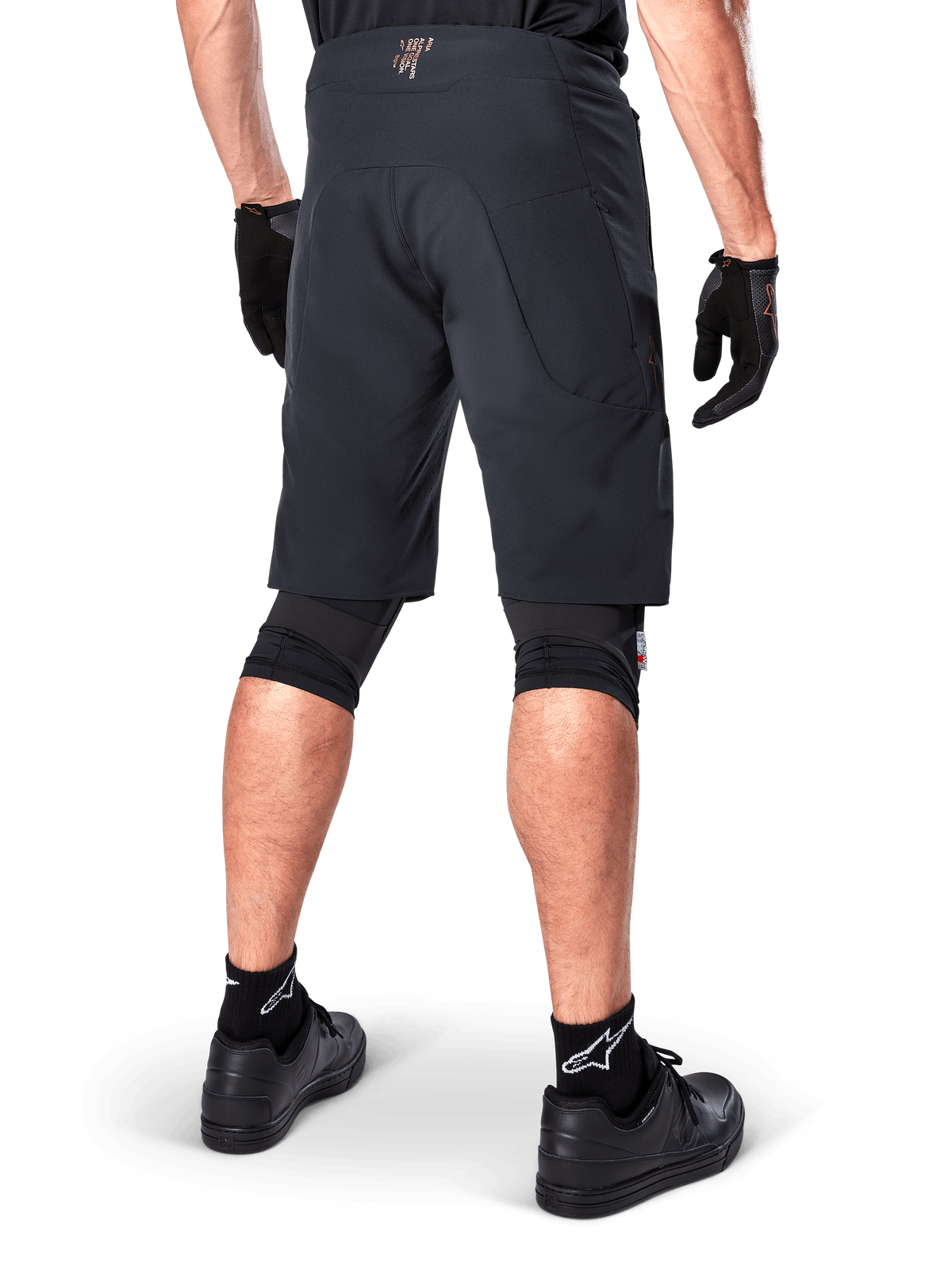 Rückansicht eines Fahrers in Alpinestars A-Aria Elite Shorts in Schwarz, Performance-Mountainbike-Shorts, kombiniert mit schwarzen Fahrradhandschuhen und schwarzen Schuhen, entwickelt für flexible Bewegungsfreiheit auf Offroad-Trails