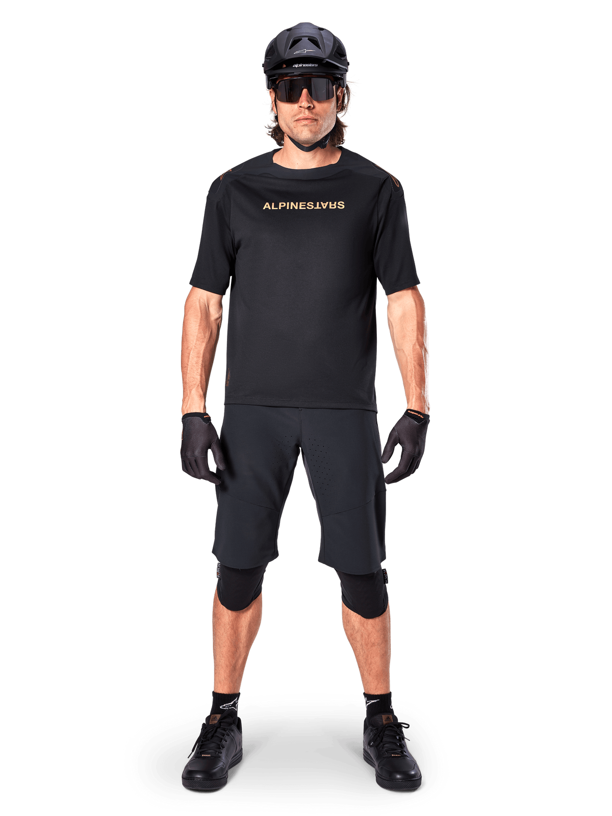 Männlicher Mountainbike-Fahrer in Alpinestars A-Aria Elite Shorts in Schwarz, kombiniert mit einem passenden schwarzen Alpinestars Kurzarmtrikot, schwarzem Helm, Handschuhen und Knieschützern, komplette Offroad-Radsportausrüstung