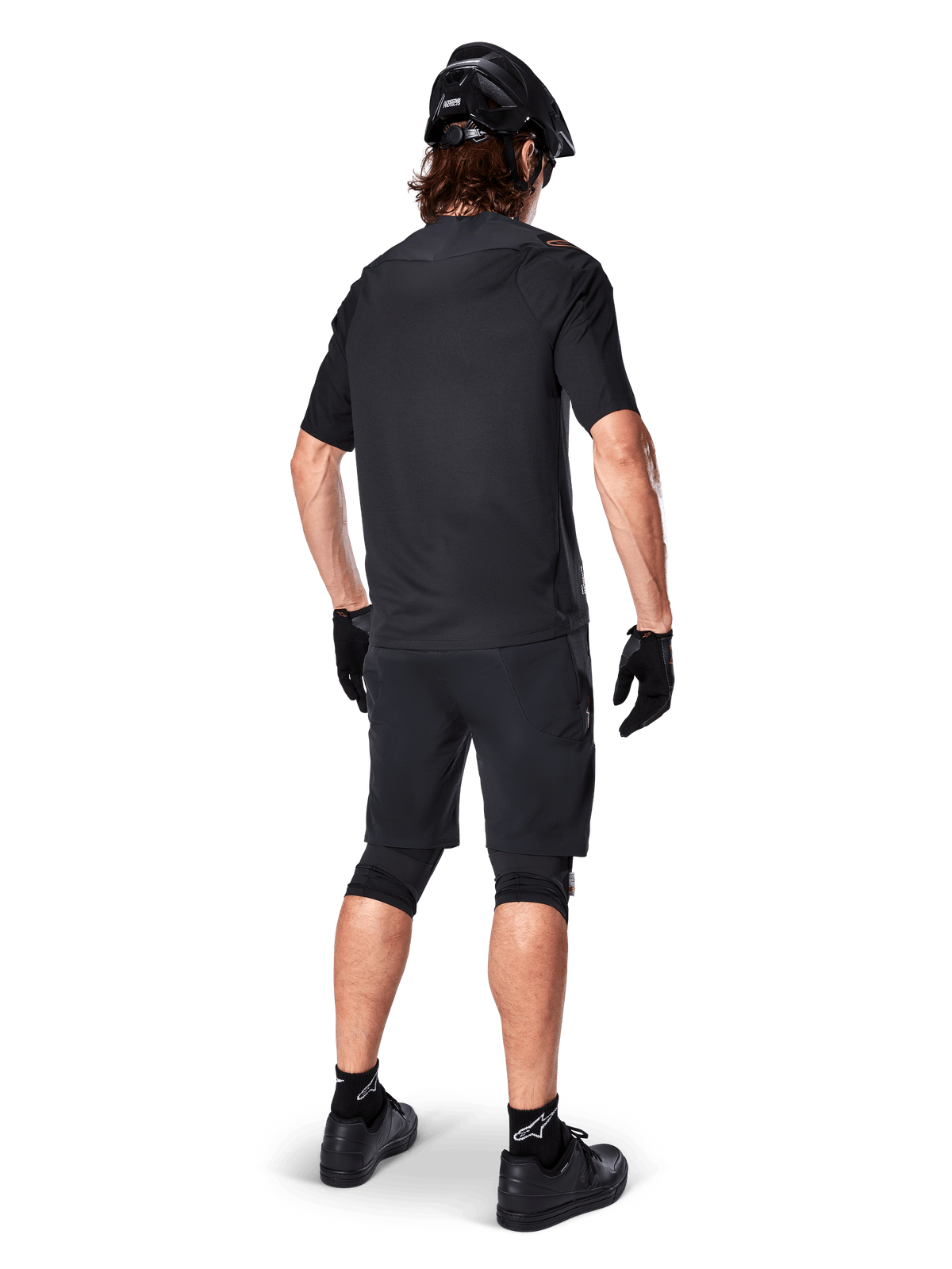 Rückansicht eines Mountainbikers in Alpinestars A-Aria Elite Shorts in Schwarz, kombiniert mit einem passenden schwarzen Kurzarmtrikot, schwarzem Helm, Handschuhen und MTB-Schuhen; zeigt ein komplettes Performance-Outfit für den Offroad-Radsport.