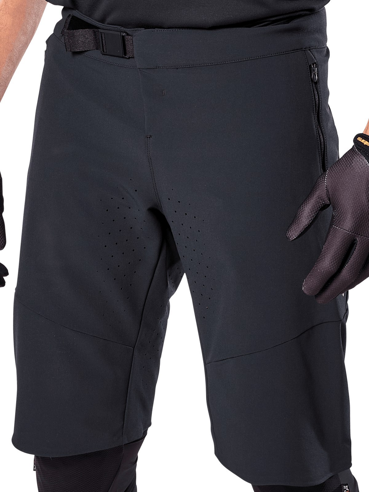 Alpinestars A-Aria Elite Shorts in Schwarz, Nahaufnahme des Taillen- und Oberschenkelbereichs, mit magnetischem Schnallenverschluss, Reißverschlusstaschen und lasergeschnittenen Belüftungsperforationen, getragen mit schwarzen Fahrradhandschuhen zum Mountainbiken.