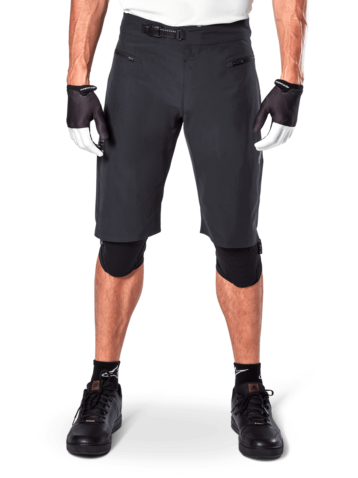 Alpinestars A-Aria Shorts, schwarze Mountainbike-Shorts mit Ratschenverschluss an der Taille und Reißverschlusstaschen, kombiniert mit schwarz-weißen Handschuhen und Knieschützern, technische Fahrradausrüstung für das Gelände