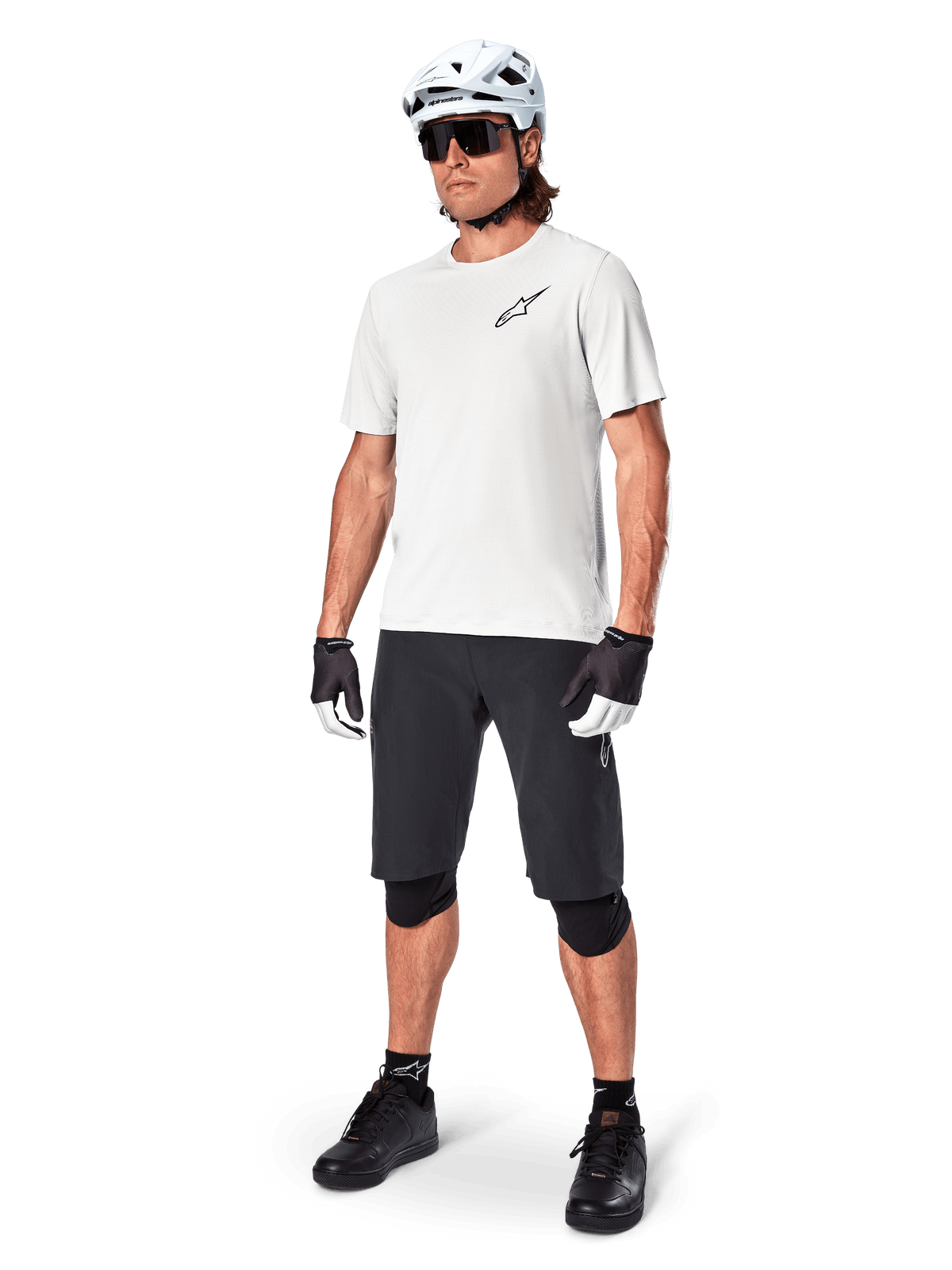 Männlicher Mountainbiker in Alpinestars A-Aria Shorts, schwarze Radsport-Shorts, kombiniert mit einem weißen Kurzarm-Trikot, weißem Mountainbike-Helm und schwarzer Performance-Ausrüstung, komplettes Outfit für Offroad-Trail-Fahrten