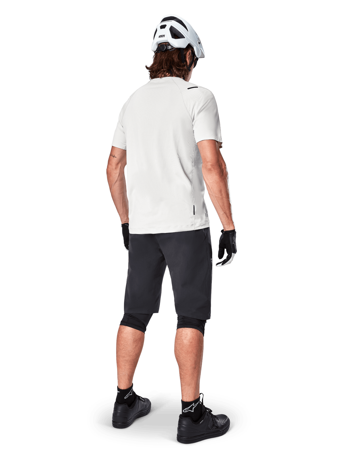 Mountainbiker von hinten in Alpinestars A-Aria Shorts in Schwarz, weißem Performance-Kurzarmtrikot, weißem Helm, schwarzen Handschuhen und schwarzen Mountainbike-Schuhen, Fahrradausrüstung für Trail-Riding