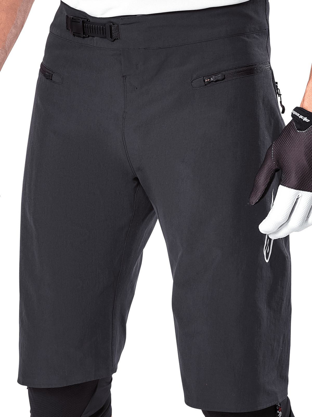 Alpinestars A-Aria Shorts, Mountainbike-Shorts, Schwarz, Nahaufnahme des Taillen- und Oberschenkelbereichs mit Ratschenverschlusssystem und Reißverschlusstaschen, getragen mit schwarz-weißen Fahrradhandschuhen, Performance-Trail-Ausrüstung