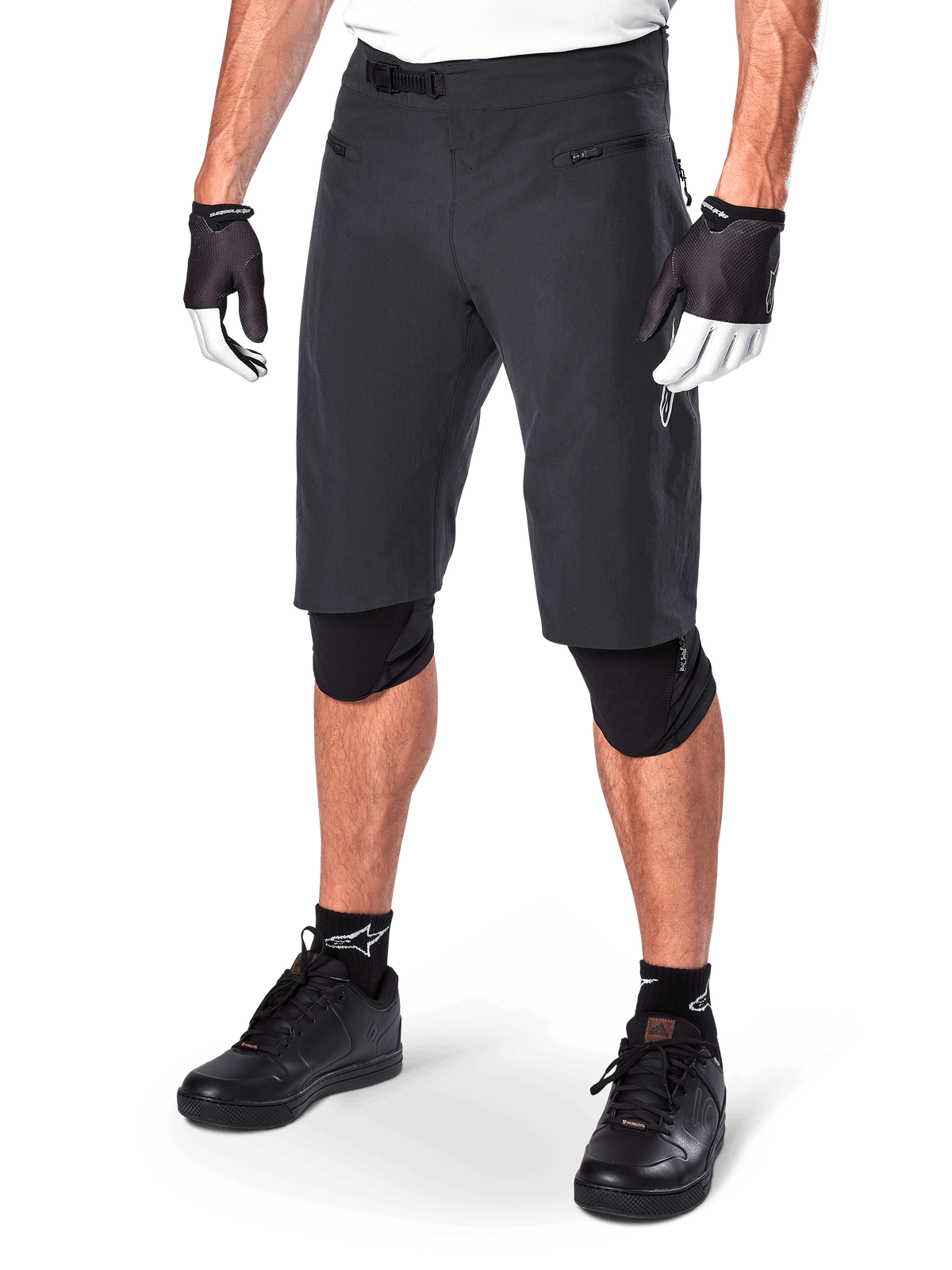 Alpinestars A-Aria Shorts, Mountainbike-Shorts, Schwarz, knielang mit vorderen Reißverschlusstaschen und verstellbarem Ratschenverschluss am Bund, getragen mit schwarzen Knieschützern, Socken und Fahrradhandschuhen