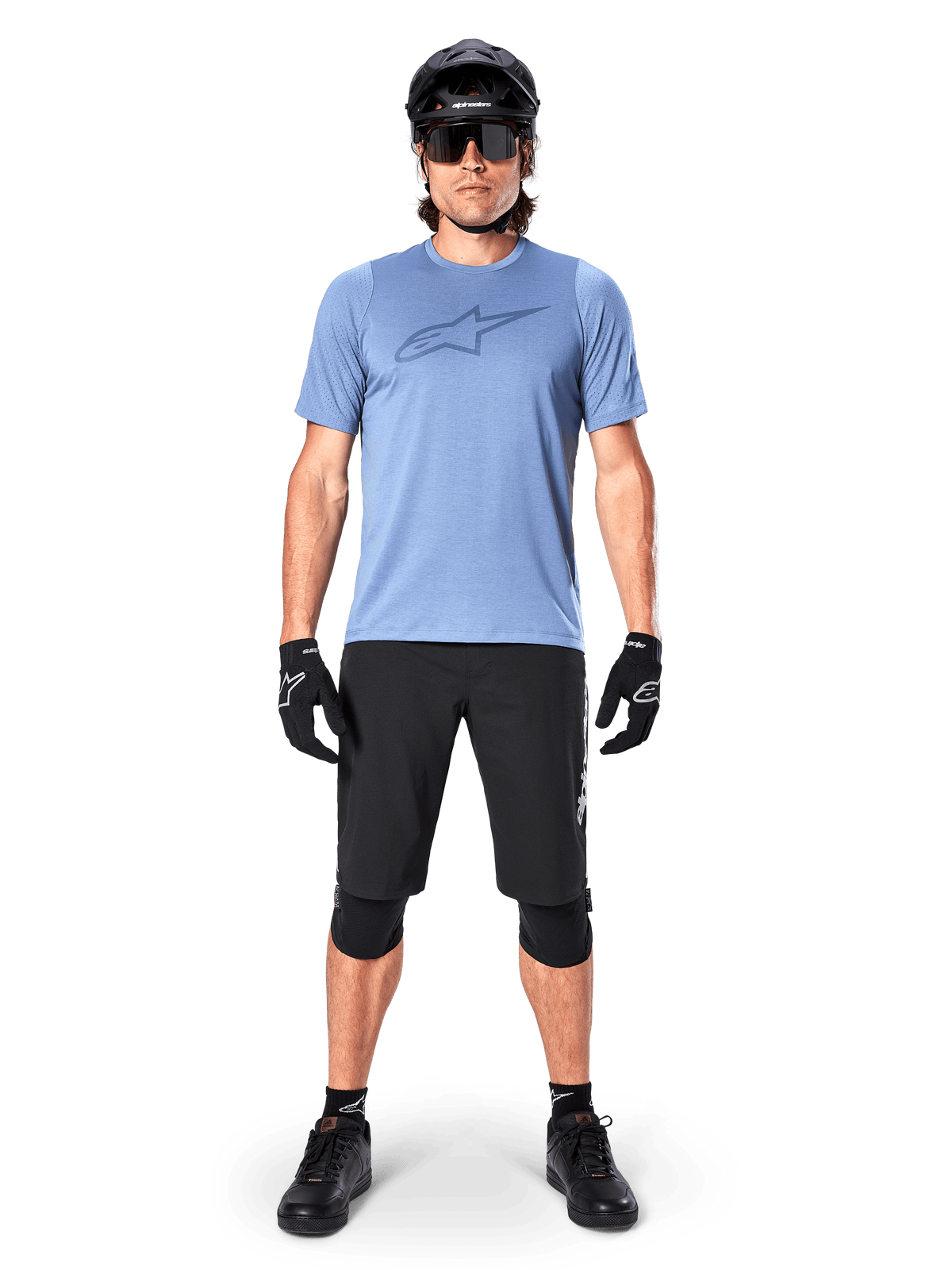 Alpinestars A-Dura Elite Shorts, schwarze Mountainbike-Shorts, getragen mit einem hellblauen T-Shirt, schwarzem Helm, Sonnenbrille und Knieschützern, professionelle Offroad-Radsportbekleidung