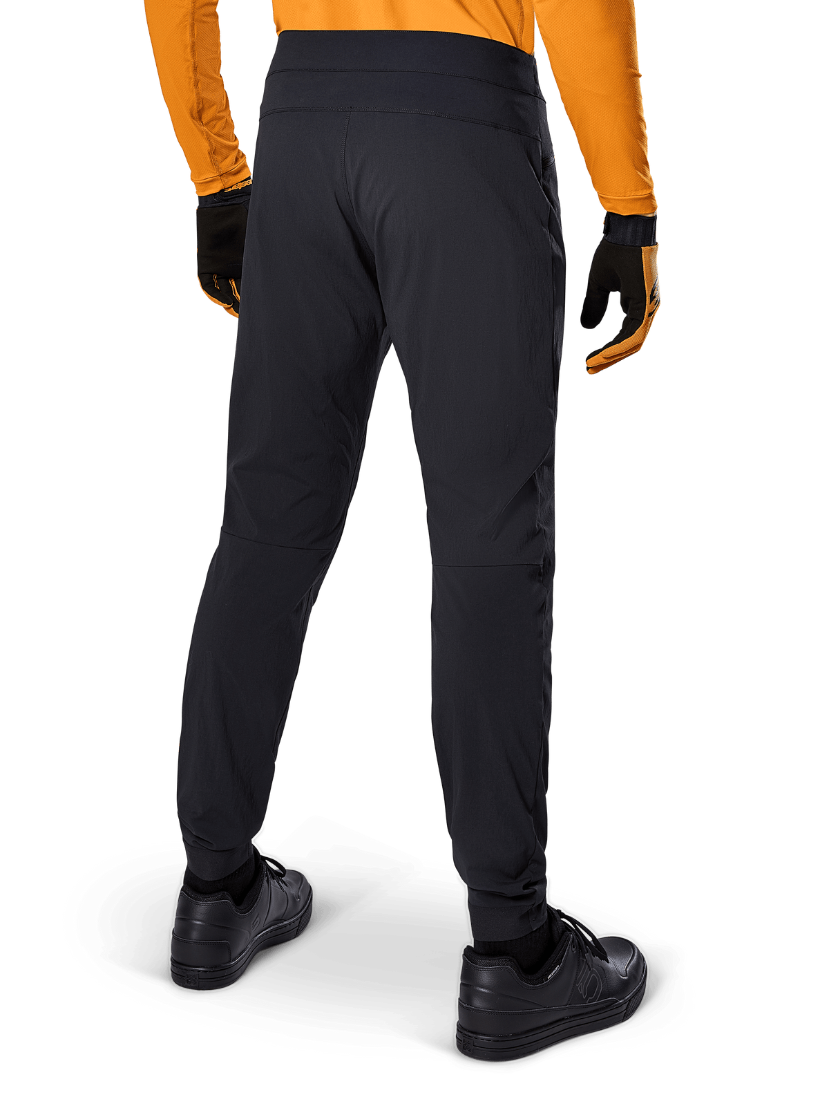 Alpinestars A-Dura Hose, schwarze MTB-Hose, Rückansicht, getragen mit einem orangefarbenen Langarm-Trikot und schwarzen Handschuhen, mit elastischen Bündchen und strapazierfähigem Textilmaterial für Mountainbiking.