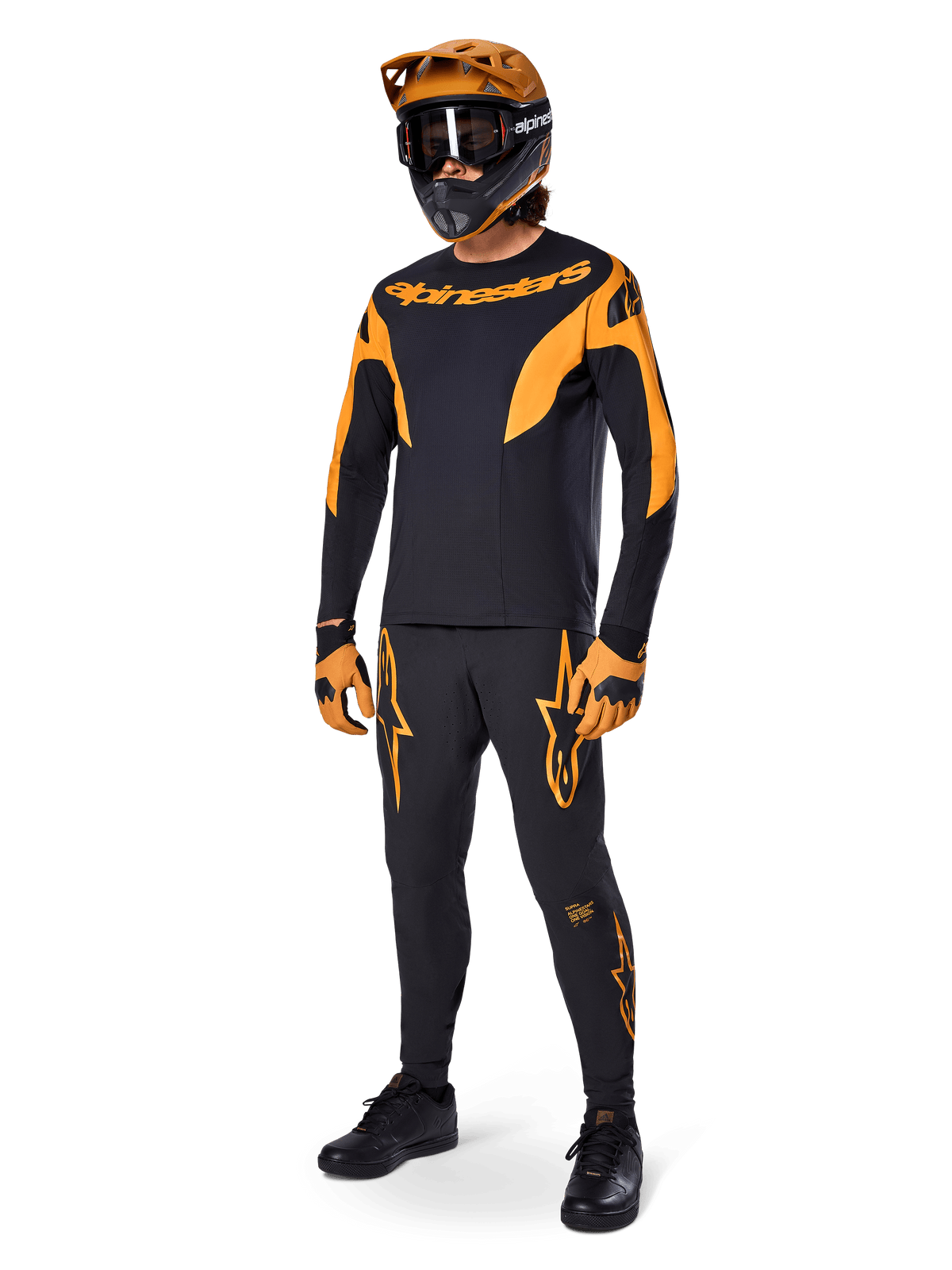 Mountainbike-Fahrer in kompletter Rennausrüstung, Alpinestars A-Supra Race Hose in Schwarz mit orangefarbenen Akzenten, passendes schwarz-orangefarbenes Langarm-Trikot, orangefarbener Helm mit schwarzer Goggle, orange-schwarze Handschuhe und schwarze Schuhe, professionelles MTB-Rennset-Design
