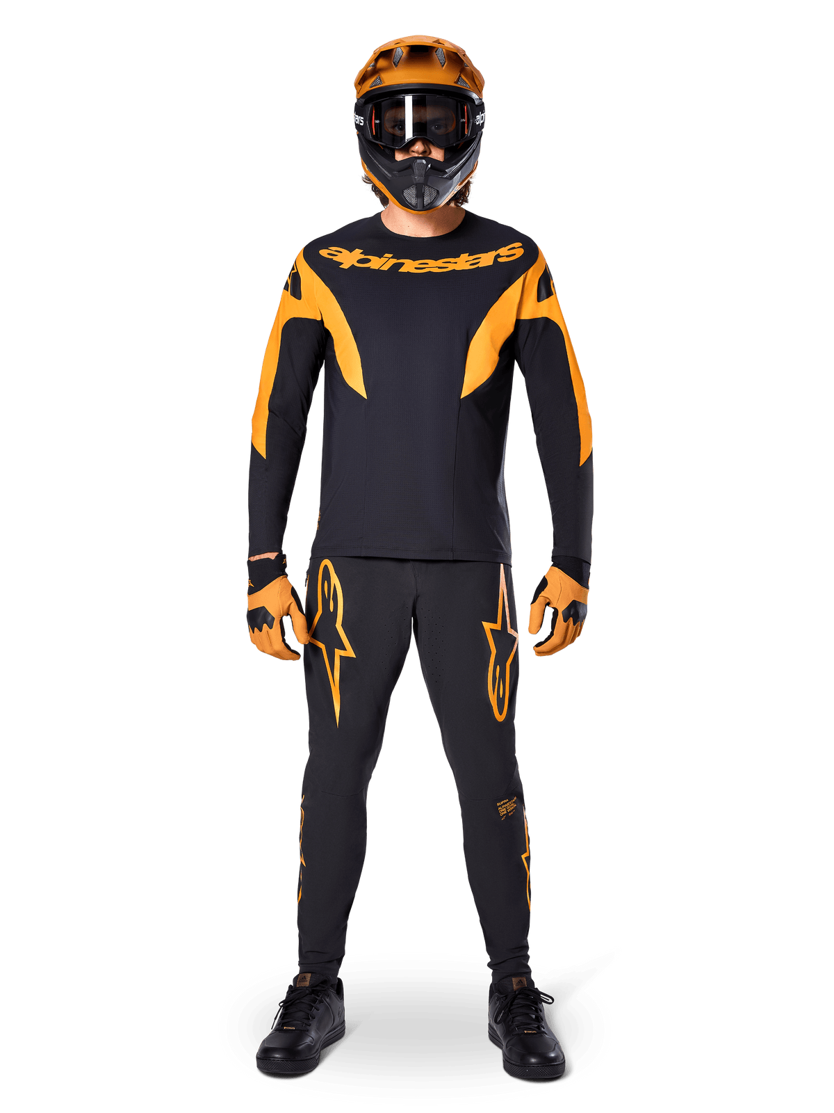 Alpinestars A-Supra Race Hose, MTB-Rennhose, Schwarz und Orange, getragen von einem Fahrer in kompletter Rennausrüstung inklusive schwarz-orangenem Trikot, orangenem Helm und passenden Handschuhen, mit markanten orangenen Stern-Logos auf den Beinen