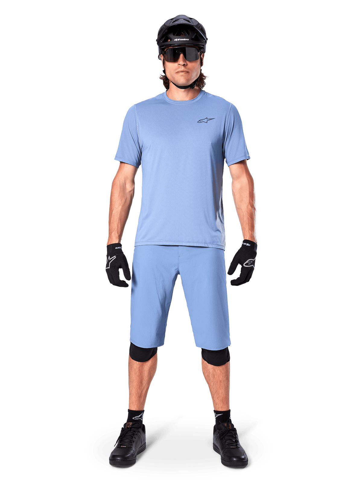 Model trägt Alpinestars A-Dura Shorts in Infinity Blue, passendes hellblaues Trikot, schwarzen Mountainbike-Helm, schwarze Sonnenbrille, schwarze Handschuhe und Knieschoner, komplettes MTB-Outfit für Trailfahrten