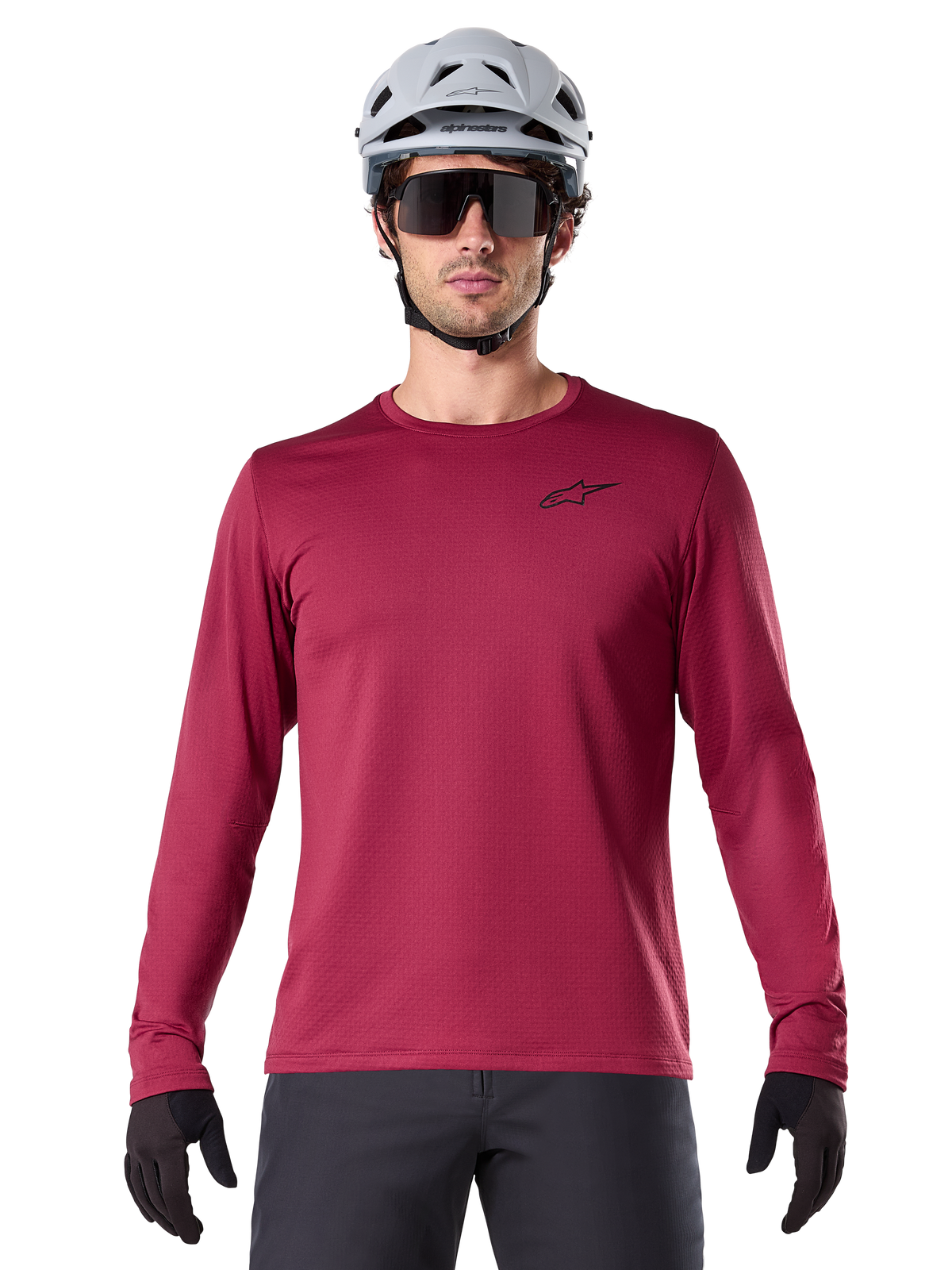 Männlicher Radfahrer trägt das Alpinestars A-Dura Thermal Jersey, langärmeliges MTB-Trikot, Burgunderrot, kombiniert mit einem grauen Helm und einer schwarzen Sonnenbrille, kleines schwarzes Stern-Logo auf der Brust, isoliertes Fleece-Material für Mountainbiking bei kaltem Wetter
