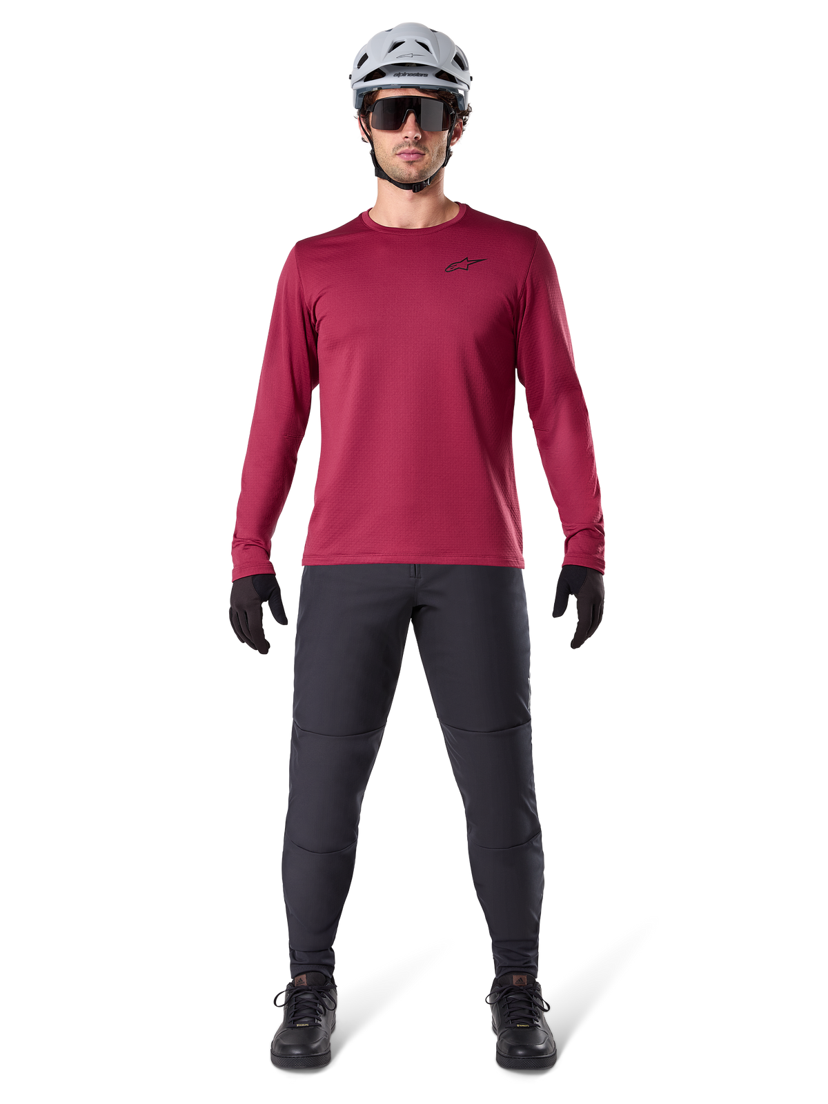 Männliches Model im Alpinestars A-Dura Thermal Jersey in Burgundy, langärmeliges isoliertes Radsport-Oberteil, kombiniert mit dunkelgrauer Mountainbike-Hose, weißem Helm, schwarzer Sonnenbrille und schwarzen Handschuhen, professionelle MTB-Ausrüstung für kaltes Wetter