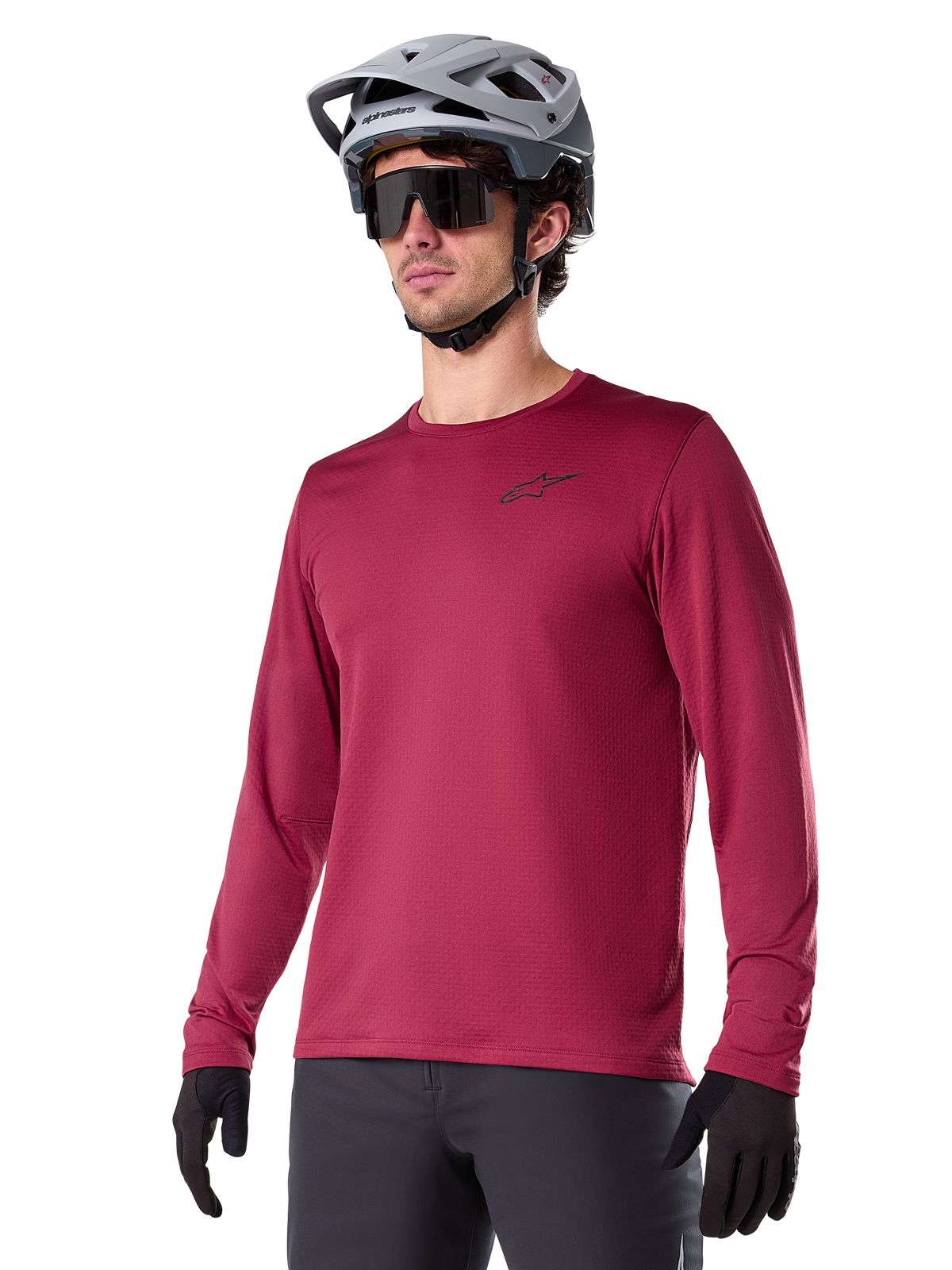 Alpinestars A-Dura Thermal Jersey, Langarm-Mountainbike-Trikot, Burgunderrot, mit isoliertem Fleece-Futter und kleinem schwarzem Brust-Logo, getragen mit einem grauen Helm, schwarzer Sonnenbrille und schwarzen Handschuhen, ideal für Radsport bei kaltem Wetter
