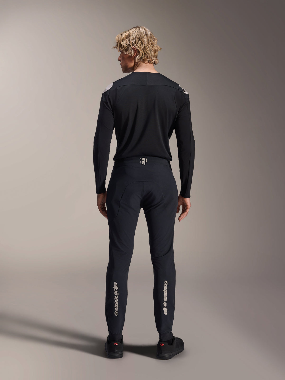 Alpinestars A-Aria Polartec Elite Langarm-Trikot, schwarzes MTB-Trikot, Rückansicht getragen mit passender schwarzer Hose, Performance-Passform für das Mountainbiken, aus technischem feuchtigkeitsableitendem Material mit dezentem Branding am unteren Rücken.