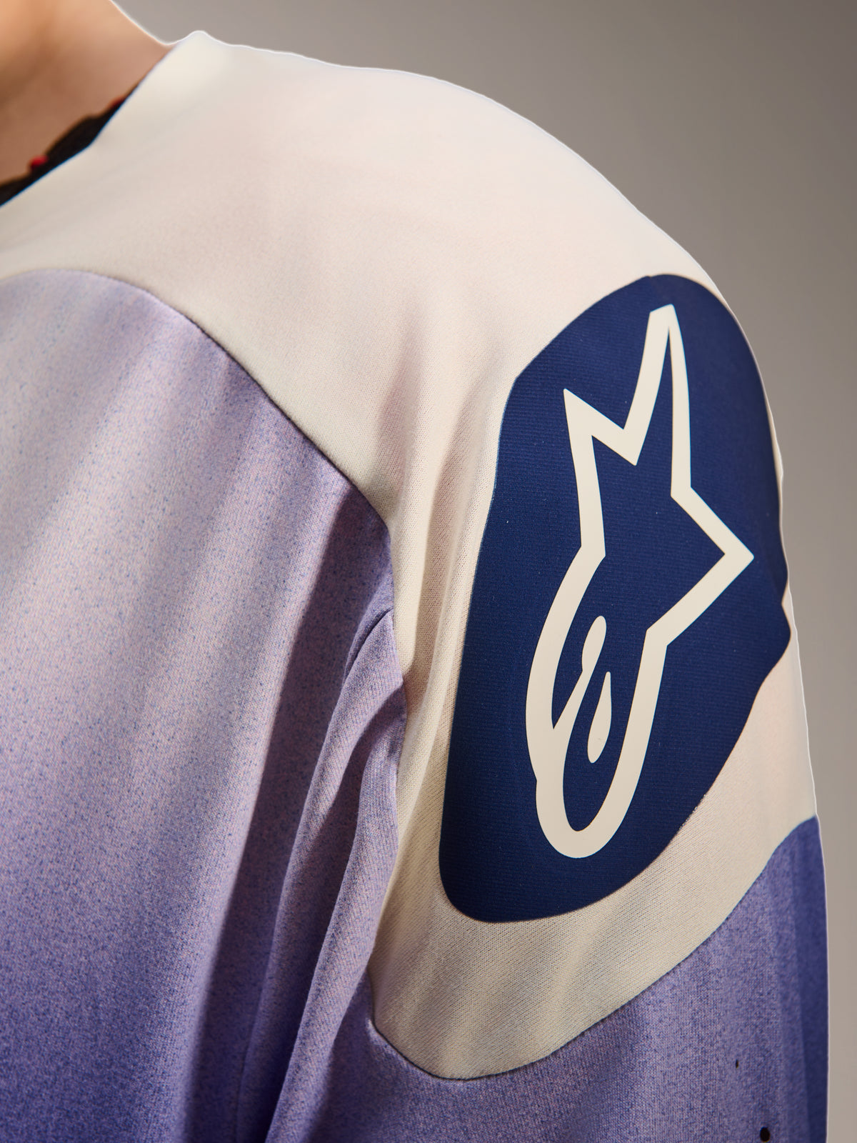 Alpinestars A-Aria Polartec Maker Elite Jersey, Langarm-Mountainbike-Trikot, Baja Blue und Weiß, Nahaufnahme der Schulter mit einem großen blauen kreisförmigen Alpinestars-Logo mit weißem Stern, zeigt Laserperforationen und technische Gewebestruktur
