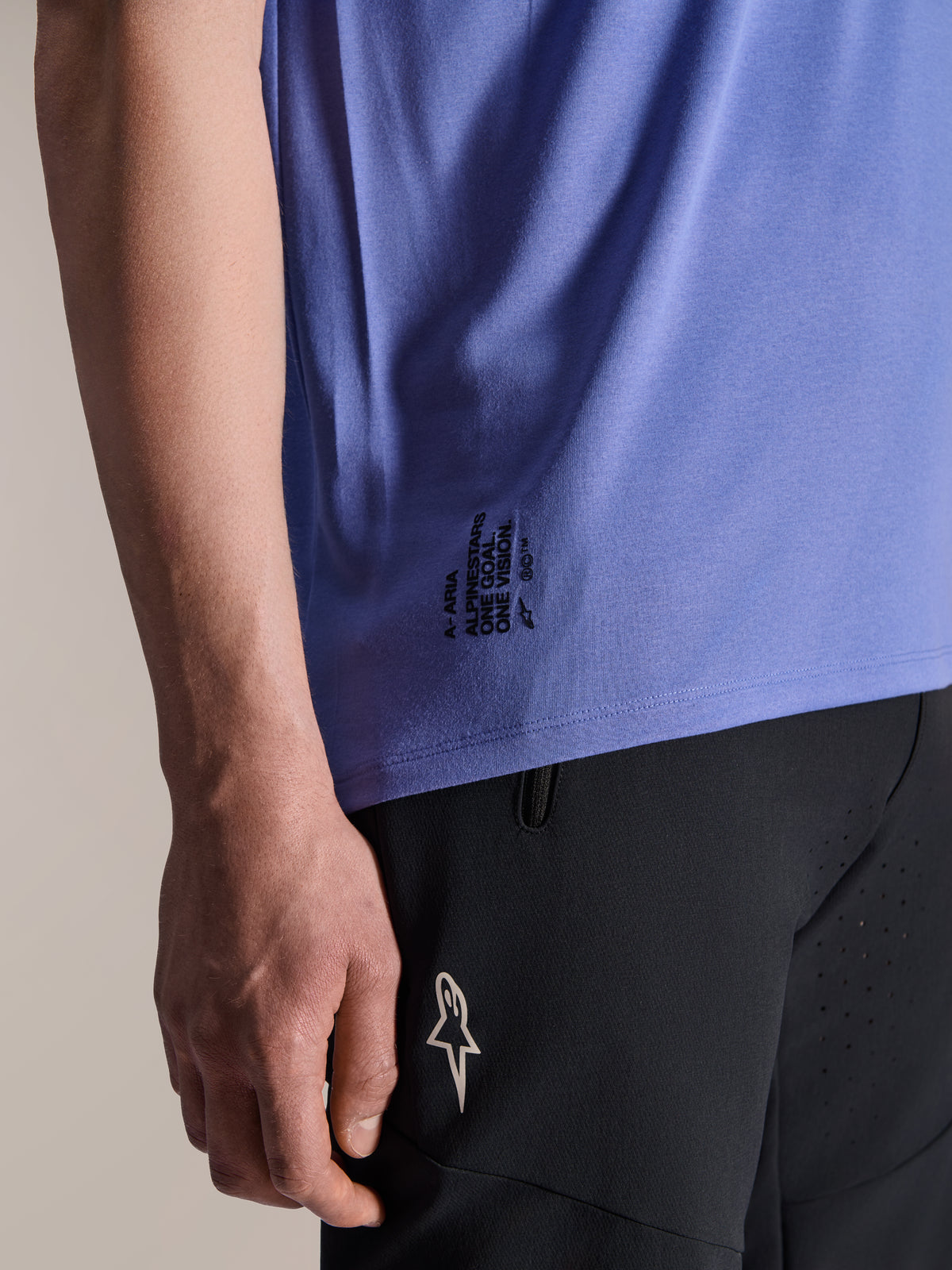 Alpinestars A-Aria Polartec Elite Kurzarmtrikot in Baja Blue, Detail des unteren seitlichen Saums mit schwarzem „One Goal. One Vision.“ Schriftzug und ASTARS-Logo-Branding, kombiniert mit schwarzen Mountainbike-Shorts.