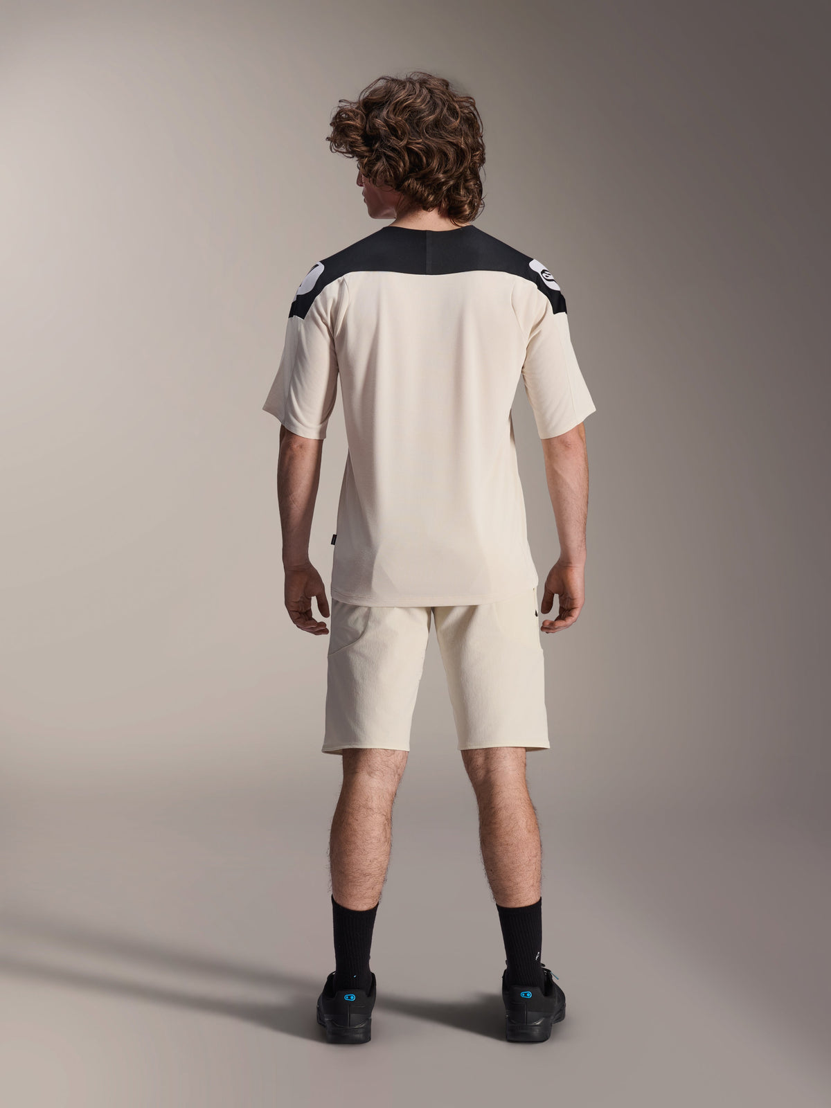 Alpinestars A-Aria Polartec Elite Kurzarmtrikot, MTB-Fahrradtrikot, Ecru mit schwarzen Schulterpartien, Rückansicht mit passenden Shorts und schwarzen Socken, Performance-Passform mit verlängertem Rückenteil für den Offroad-Einsatz.