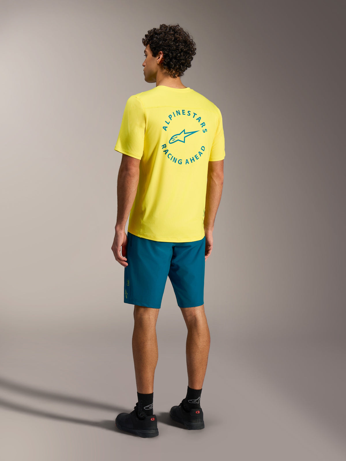 Alpinestars A-Dura Ride Shorts in Blaugrün mit gelbem Trikot, Rückansicht von Mountainbike-Performance-Ausrüstung.