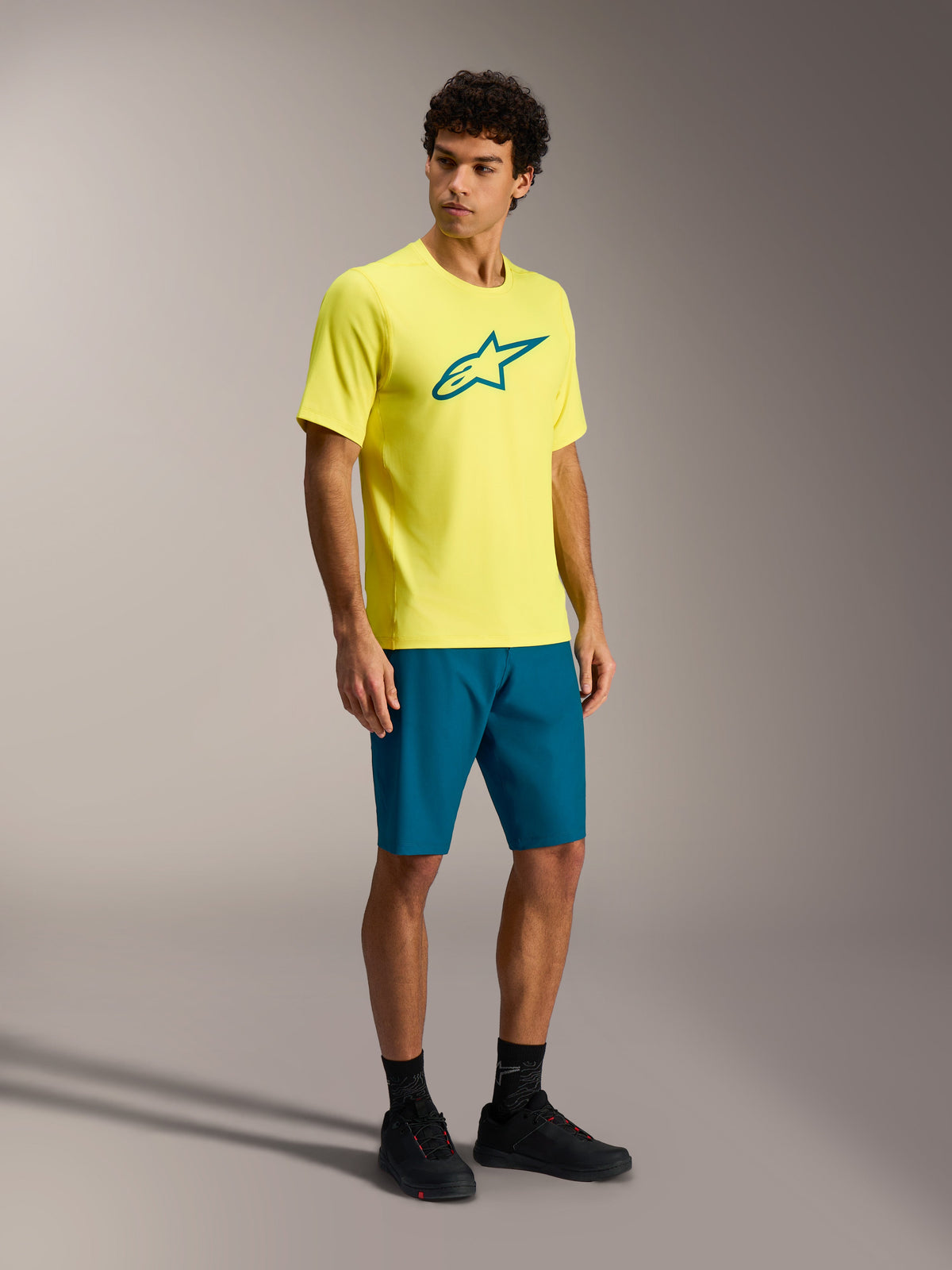 Alpinestars A-Dura Ride MTB-Outfit, gelbes Kurzarmtrikot und blaugrüne Shorts an einem männlichen Model.