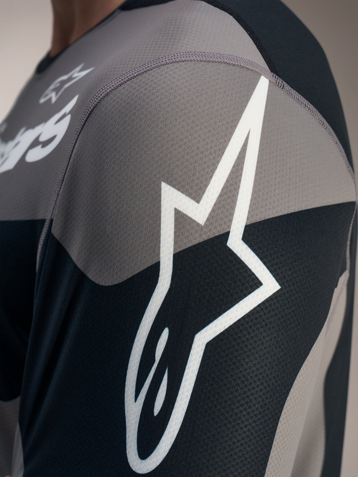Graues A-Dura Race Langarmtrikot, Detail des weißen Astars-Logos auf technischem Jacquard-Mesh-Gewebe.