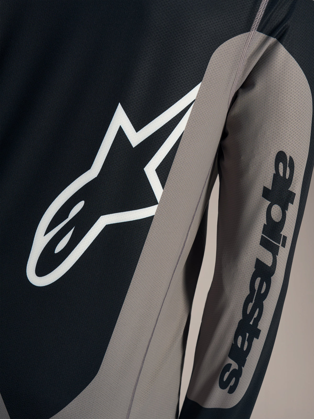 Graues A-Dura Race Langarmtrikot, Detail mit weißem Astars-Logo und Alpinestars-Schriftzug am Ärmel.