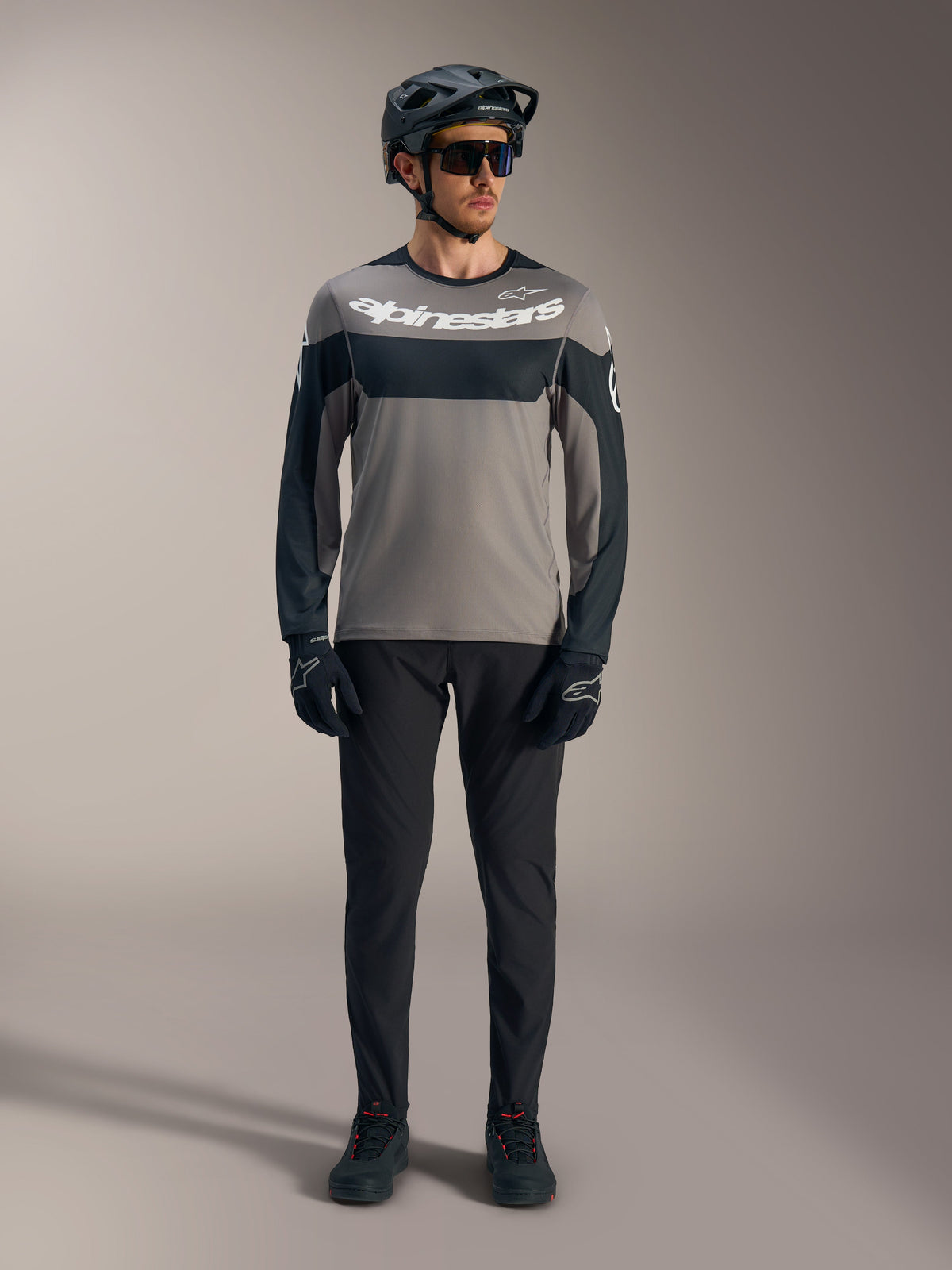 A-Dura Race Langarmtrikot in Grau und Schwarz mit weißem Alpinestars-Logo, kombiniert mit MTB-Performance-Ausrüstung.
