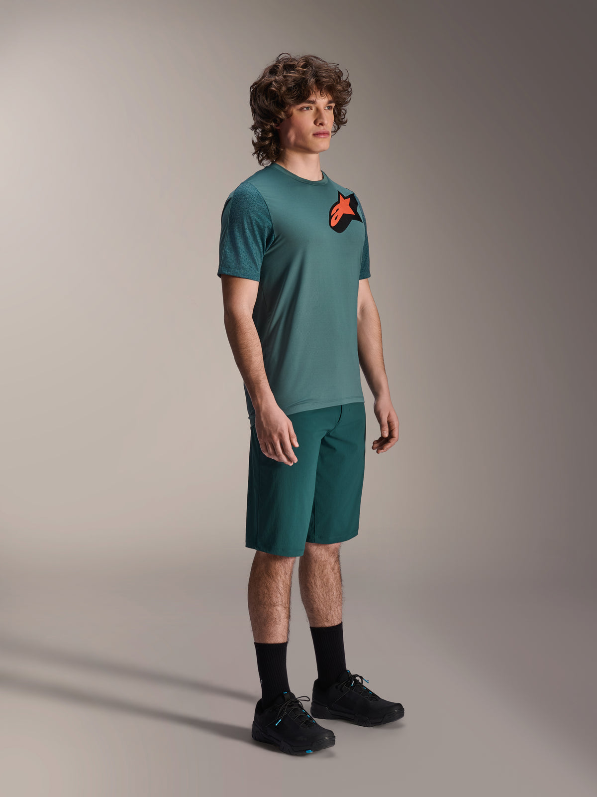 Alpinestars A-Dura Lipan SS Trikot und A-Dura Shorts, MTB-Radfahroutfit, Dark Pine, Trikot mit einem großen orangefarbenen Stern-Logo, kombiniert mit passenden Shorts und schwarzem Schuhwerk, Performance-Mountainbike-Bekleidung