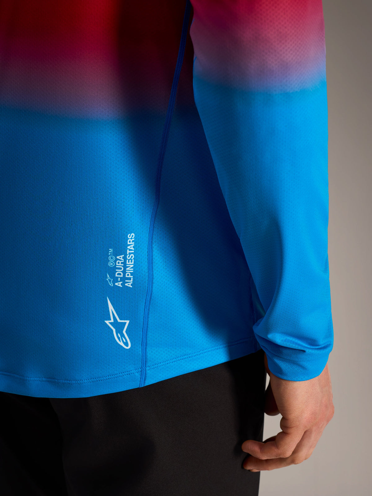 A-Dura ASTARS Langarmtrikot 2.0 mit rot-blauem Farbverlauf und weißem Alpinestars Logo-Branding an der Seite.