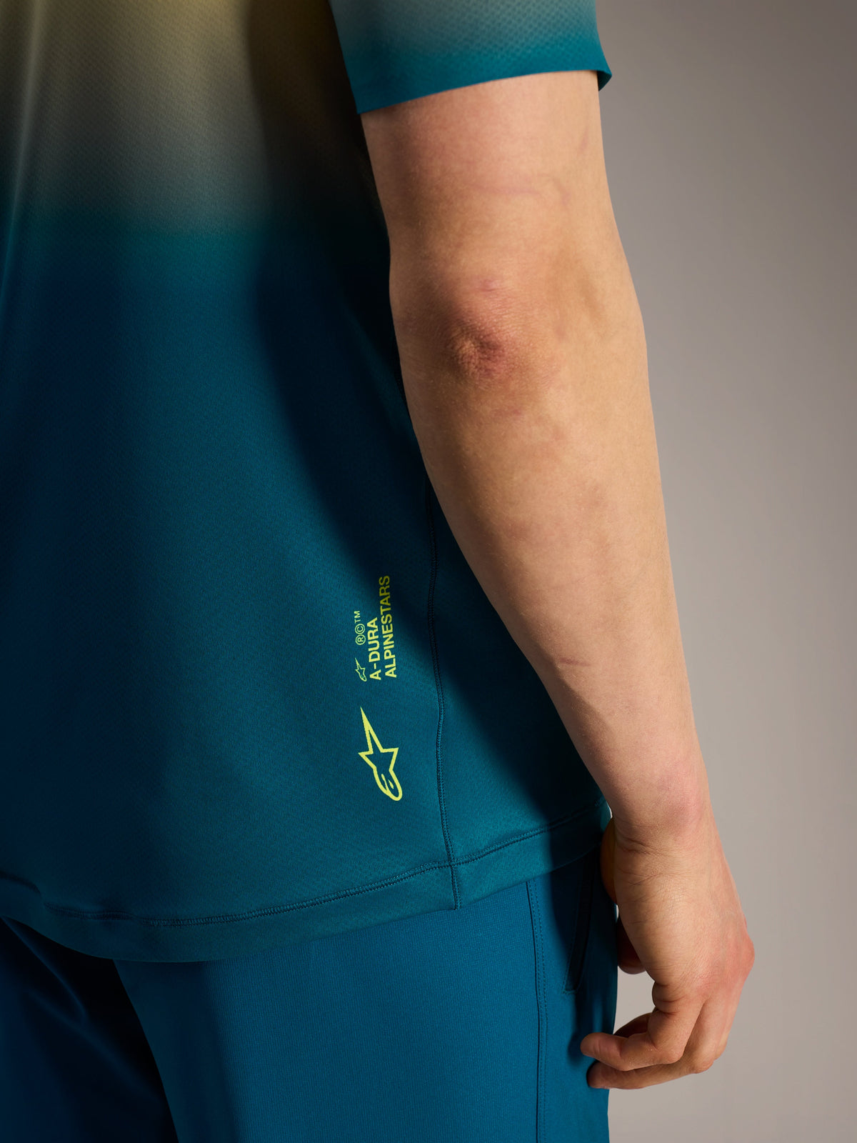 Alpinestars A-Dura ASTARS Jersey 2.0 Detail in Blaugrün mit neongelbem Logo und Branding an der Seite.