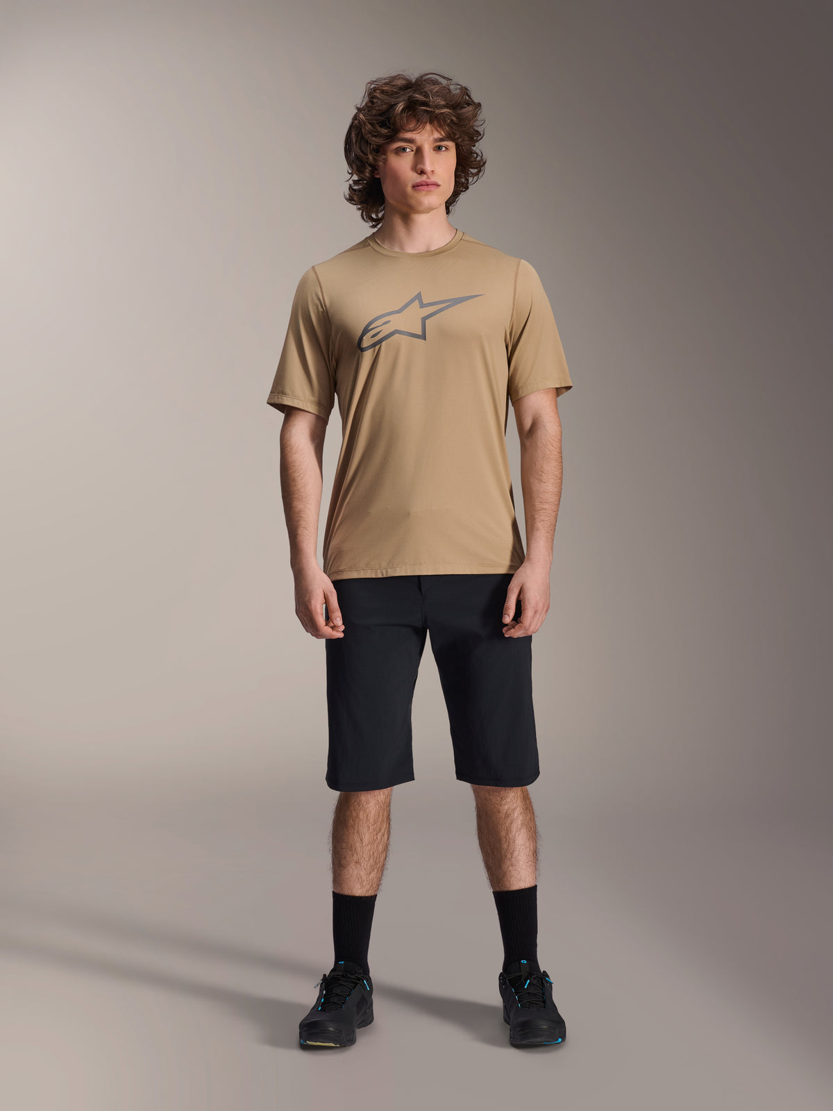 Alpinestars A-Dura Liner Shorts, MTB-Shorts, Schwarz, getragen mit beigem Kurzarm-Jersey mit grauem Stern-Logo, schwarzen Socken und Mountainbike-Schuhen, lässiges sportliches Styling