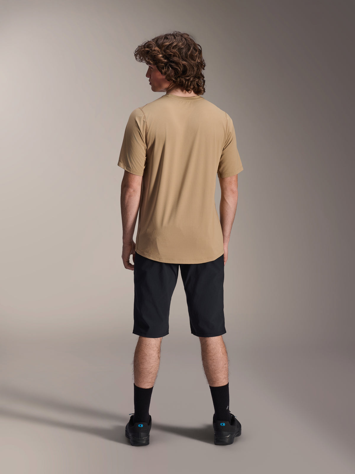Männliches Model in der Rückansicht, trägt Alpinestars A-Dura Liner Shorts in Schwarz und ein hellbraunes Kurzarm-Trikot, kombiniert mit schwarzen Socken und Schuhen, strapazierfähige Mountainbike-Bekleidung für Offroad-Radfahren.