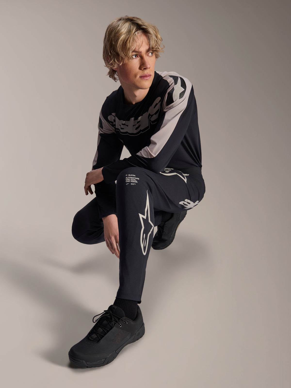 Alpinestars A-Supra Melt Pants and Long Sleeve Jersey, Black and Grey, featuring bold white branding and star logos, worn by a male model in a crouching pose, coordinated MTB racing gear