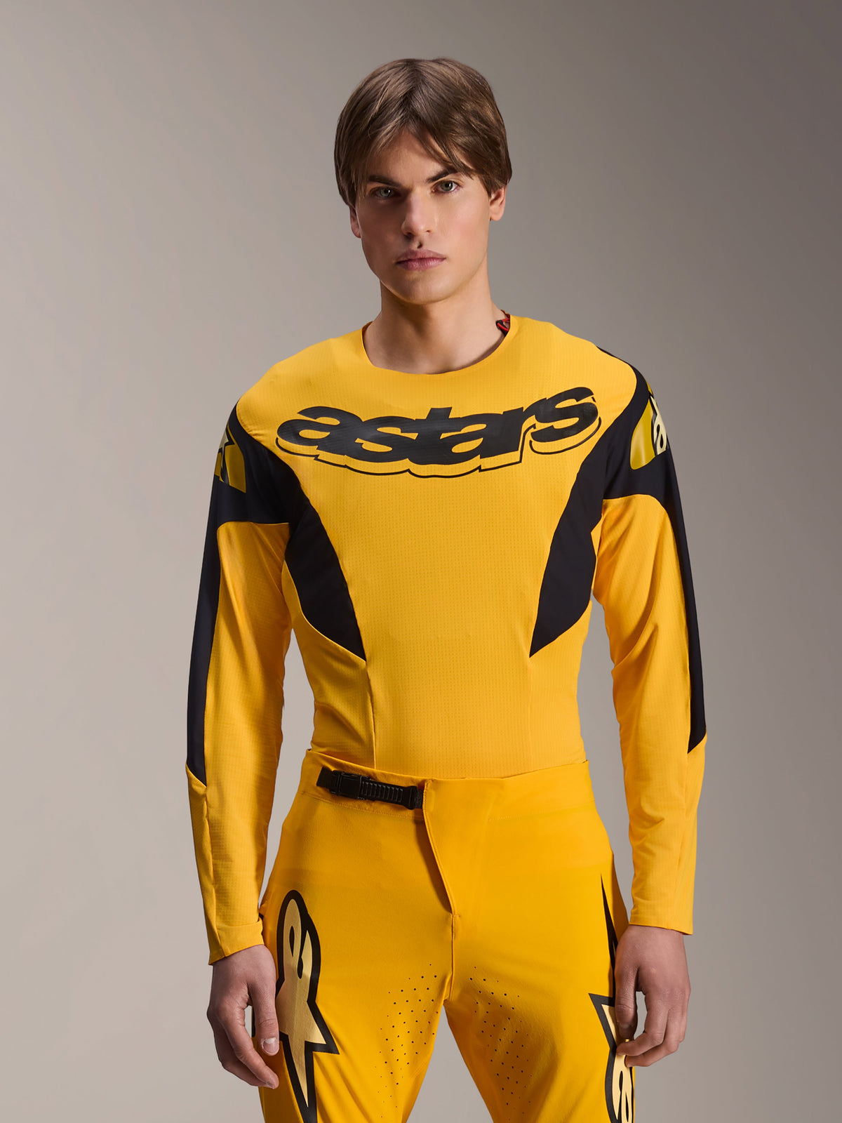 Alpinestars Limited Edition A-Supra Melt Gold Jersey, Langarm-MTB-Jersey, Dunkelgelb mit schwarzen Akzenten, getragen von einem Model mit passender Hose, mit großem schwarzem „astars“-Logo auf der Brust und athletischem Performance-Design