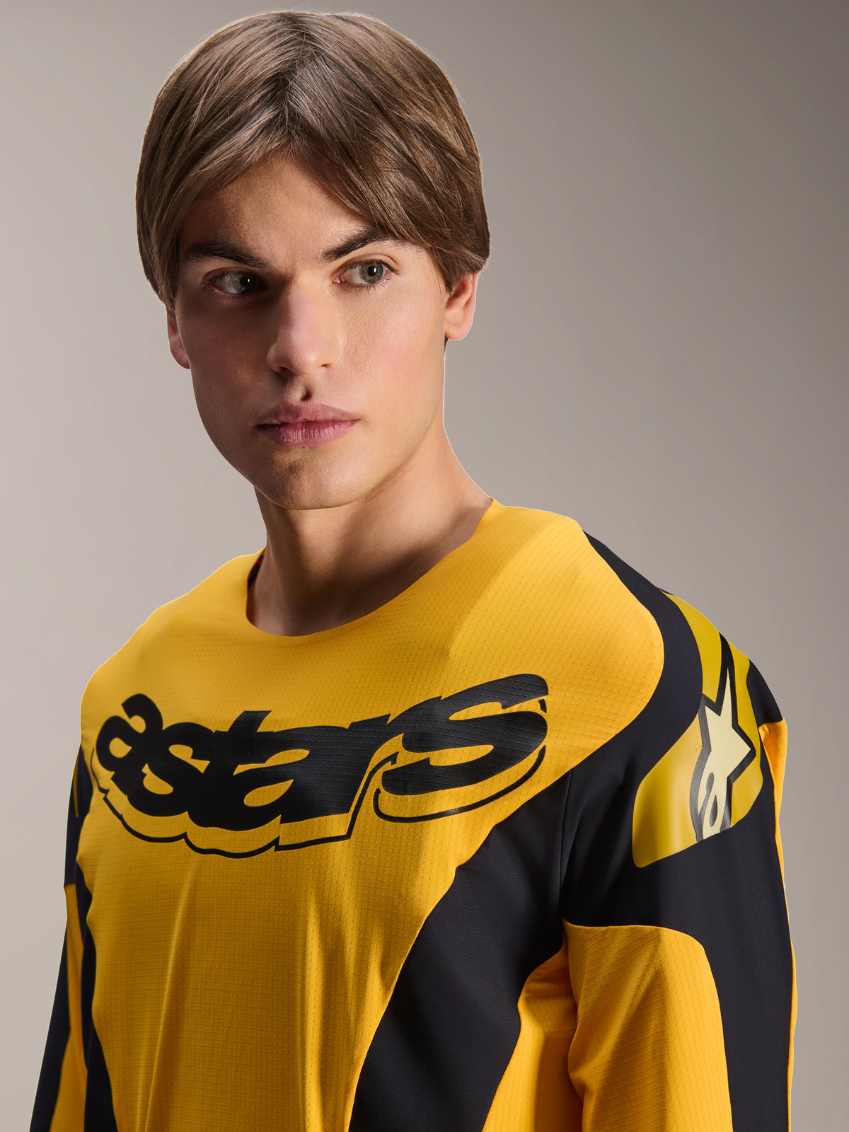 Alpinestars Limited Edition A-Supra Melt Gold Trikot, Langarm-MTB-Trikot, Dunkelgelb mit schwarzen, vom Rennsport inspirierten Grafiken, schwarzer „astars“-Schriftzug auf der Brust und Stern-Logo auf der Schulter, getragen von einem männlichen Model