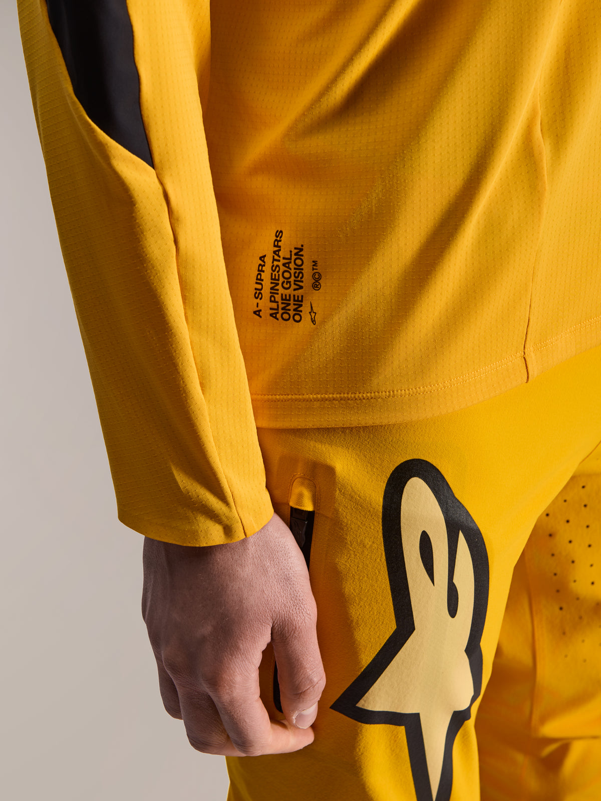 Alpinestars Limited Edition A-Supra Melt Gold Hose und passendes Langarm-Trikot, Dunkelgelb, Nahaufnahme mit „One Goal. One Vision.“ Branding und großem stilisiertem Logo auf dem Oberschenkel, Hochleistungs-MTB-Ausrüstung