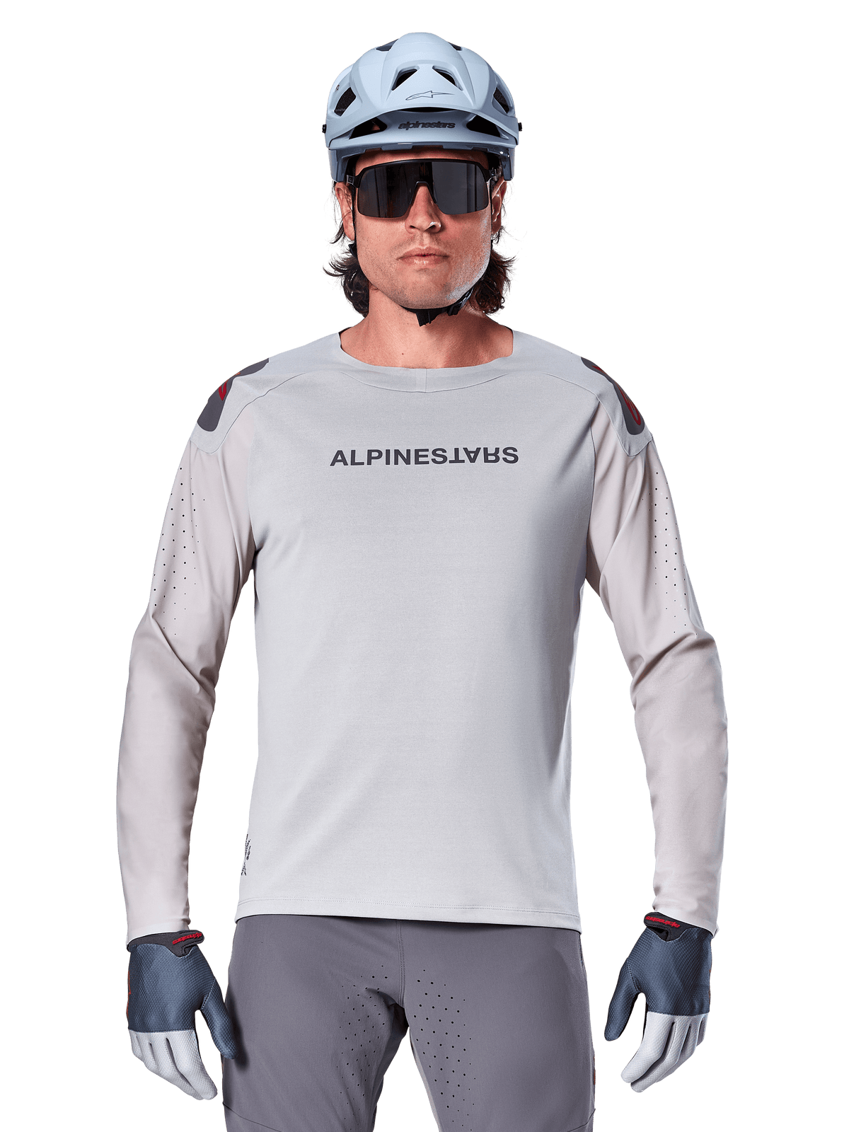 Alpinestars A-Aria Polartec Switch Langarmtrikot, hellgraues Mountainbike-Trikot mit Laserperforationen an den Ärmeln und Branding auf der Brust, getragen mit hellblauem Helm, Sonnenbrille und grauen Handschuhen