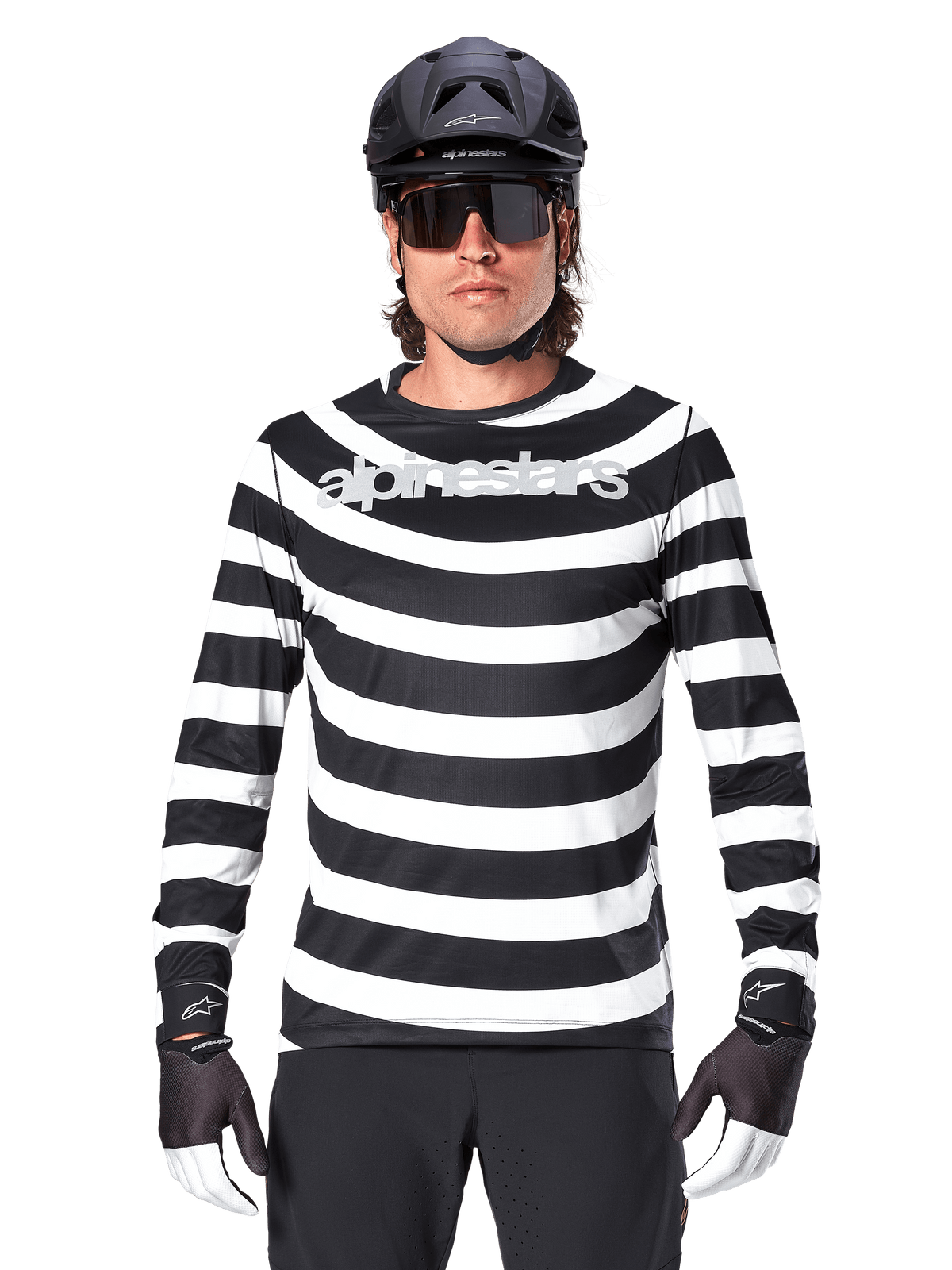 Alpinestars A-Aria Oscar Langarmtrikot, Schwarz und Weiß horizontal gestreift, reflektierendes Alpinestars-Logo auf der Brust, getragen von einem männlichen Radfahrer mit schwarzem MTB-Helm, Fahrradsonnenbrille und Performance-Handschuhen