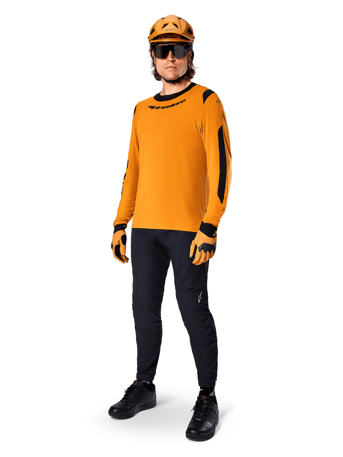 Alpinestars A-Dura Dri Wool Langarmtrikot, Dark Gold, getragen mit passendem orangefarbenem Helm, schwarzer MTB-Hose und gelb-schwarzen Handschuhen, komplettes Radsport-Outfit für Offroad-Trailfahrten