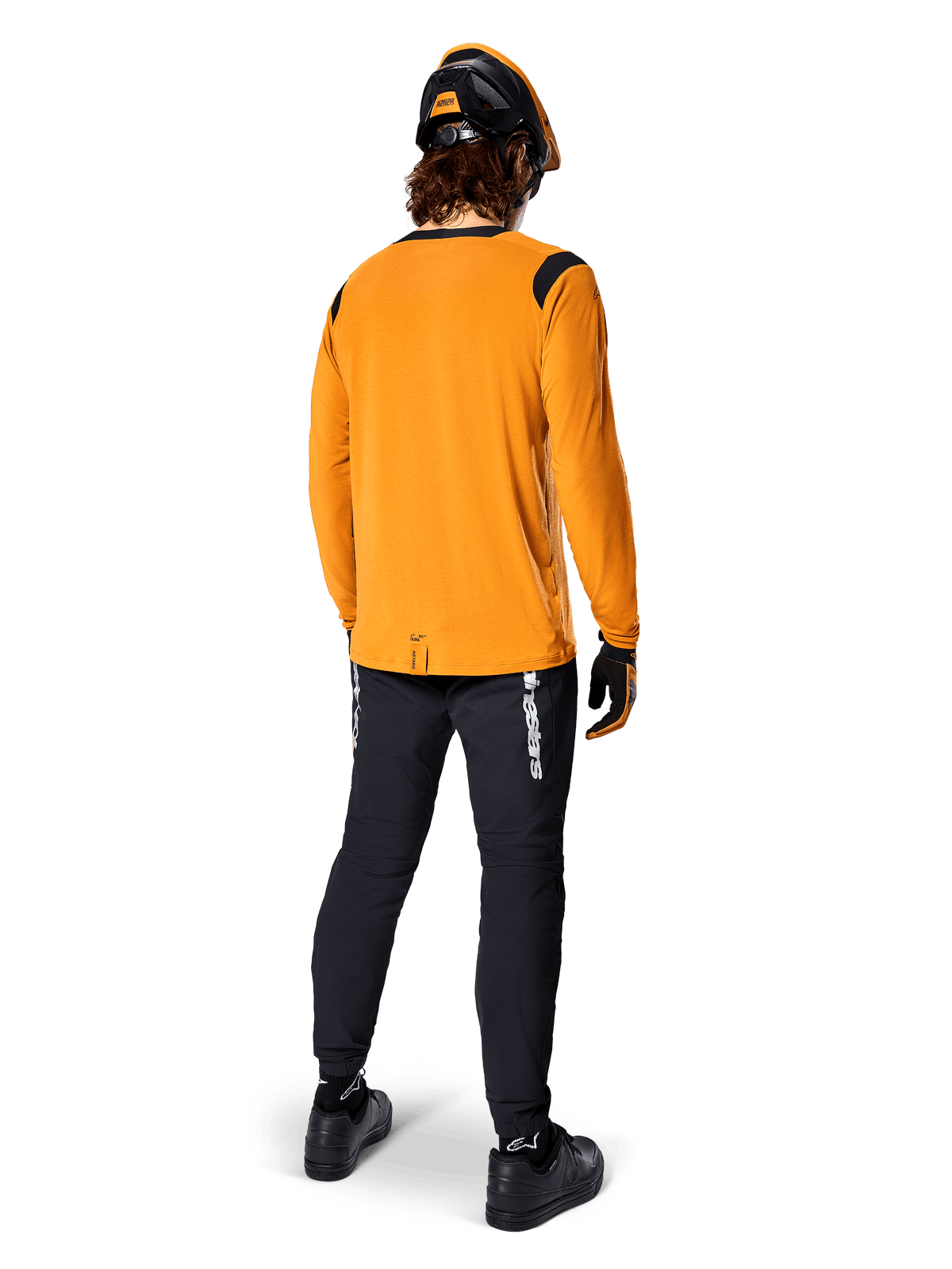 Mountainbiker von hinten gesehen im Alpinestars A-Dura Dri Wool Langarmtrikot in Dark Gold, schwarze technische Hose mit weißem Branding und passendem schwarz-orangenem Helm, leistungsorientierte Mountainbike-Bekleidung.