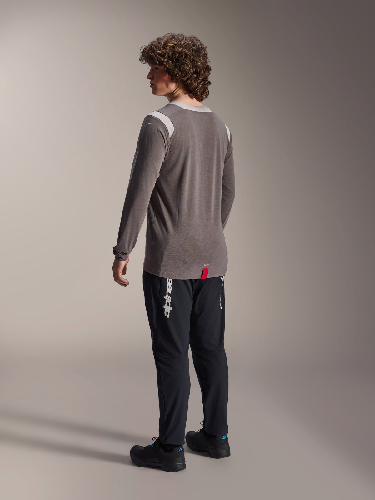 Alpinestars A-Dura Dri-Wool Langarm-Trikot in Grau kombiniert mit der A-Dura Elite Hose in Schwarz, Rückansicht des Modells, mit weißem Alpinestars-Logo am Bein, technische Mountainbike-Ausrüstung für den Offroad-Einsatz