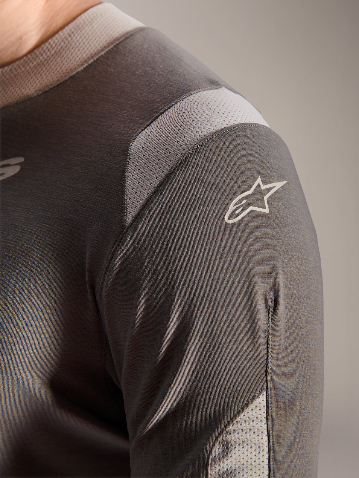 Alpinestars A-Dura Dri Wool Langarmtrikot, Dunkelgrau, Detailansicht der Schulter und des Ärmels mit hellgrauen Mesh-Belüftungseinsätzen und weißem Astars-Logo auf dem technischen drirelease-Gewebe.