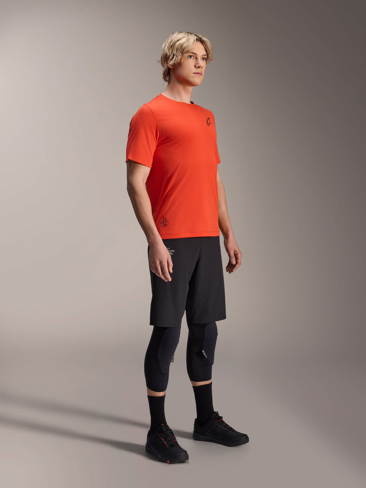 Alpinestars A-Aria Astar Kurzarmtrikot in Spicy Orange, getragen von einem Model mit schwarzen MTB-Shorts und Knieschutz, leichte, atmungsaktive Mountainbike-Bekleidung, kräftiges Orange mit minimalem schwarzem Branding