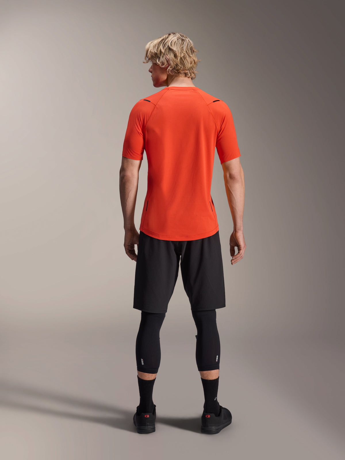 Alpinestars A-Aria Astar Trikot, Kurzarm-MTB-Trikot, Spicy Orange, Rückansicht mit Performance-Passform und längerem abfallendem Saum, kombiniert mit schwarzen Radshorts und Leggings