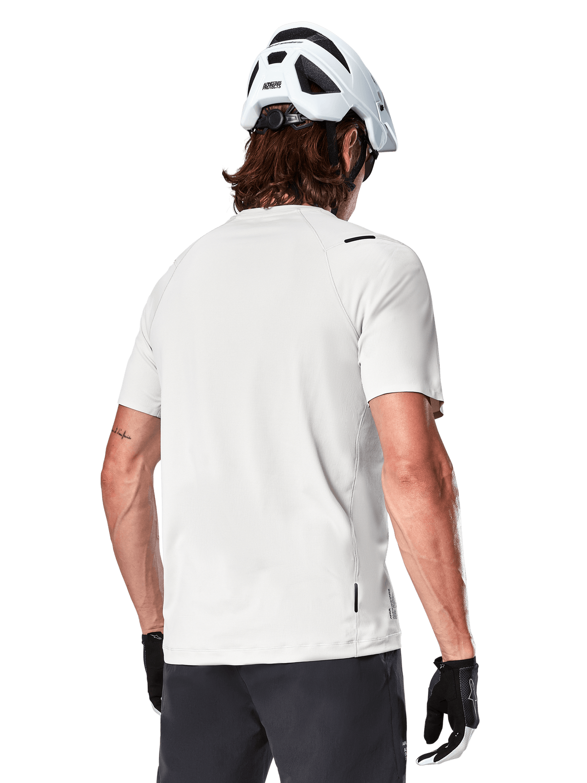 Alpinestars A-Aria Astar Trikot, Kurzarm, White Dove, Rückansicht eines leichten, atmungsaktiven Mountainbike-Trikots, getragen mit einem weißen Helm und schwarzen Fahrradhandschuhen, mit verlängertem Saum für zusätzliche Abdeckung
