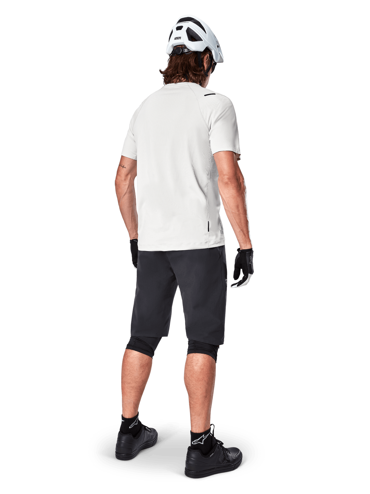 Radfahrer im Alpinestars A-Aria Astar Kurzarmtrikot in White Dove, Rückansicht, kombiniert mit schwarzen MTB-Shorts, Knieschützern und weißem Helm, leichte und atmungsaktive Ausrüstung für das Gelände