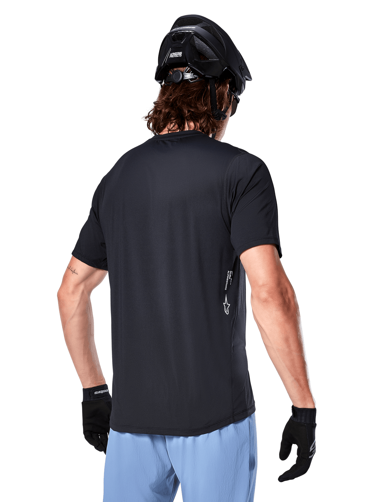 Alpinestars A-Dura Oscar Trikot, Kurzarm-Fahrradtrikot, Schwarz, Rückansicht am Fahrer, kombiniert mit hellblauen Shorts und schwarzem MTB-Helm, kleines weißes Logo an der Seite, Performance-Bekleidung für Mountainbiking