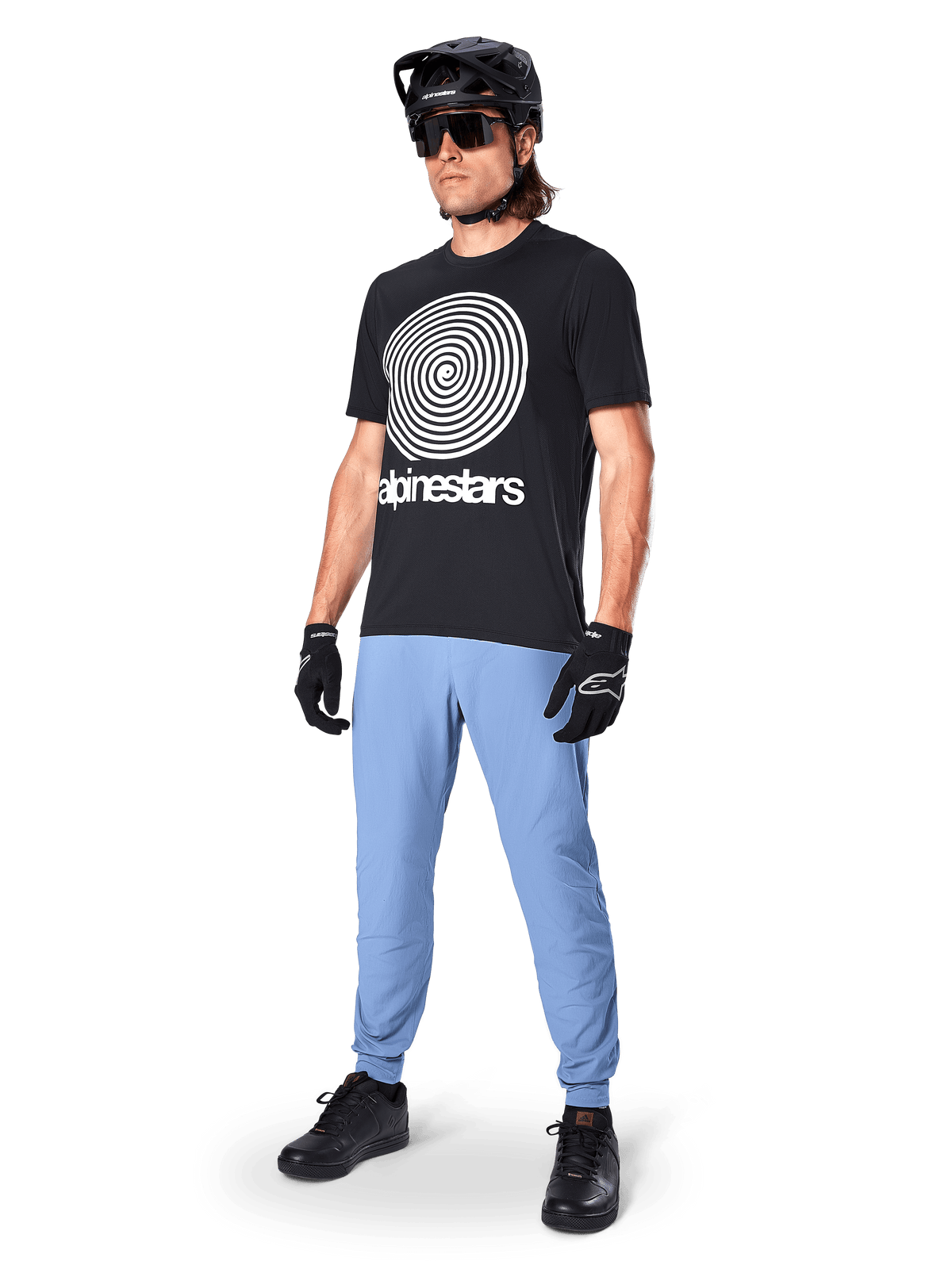 Alpinestars A-Dura Oscar Kurzarmtrikot, schwarzes MTB-Trikot mit einer großen weißen Heritage-Spiralgrafik, getragen von einem Fahrer mit schwarzem Helm, Sonnenbrille, schwarzen Handschuhen und hellblauer Hose, Performance-Mountainbike-Ausrüstung