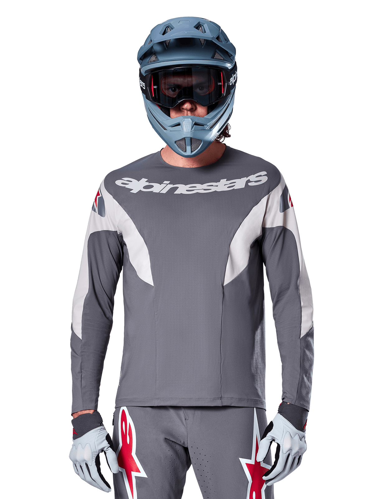 MTB rider wearing Alpinestars A-Supra Race Jersey - Long Sleeve in Dark Gray, long-sleeve cycling jersey with white Alpinestars branding, paired with a blue-gray full-face helmet, goggles, and gray racing gloves, complete mountain bike racing gear for off-road performance
