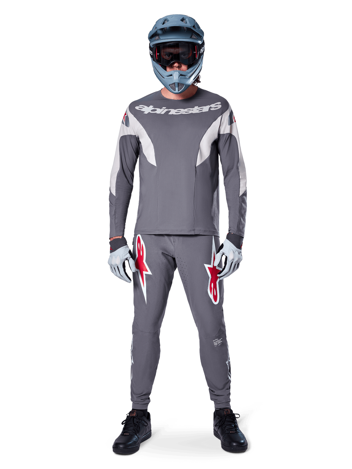 Rider wearing the Alpinestars A-Supra Race Jersey - Long Sleeve in Dark Gray, coordinated with matching gray pants featuring bold red star logos, gray helmet with goggles, and light gray gloves, complete MTB racing kit for performance off-road cycling